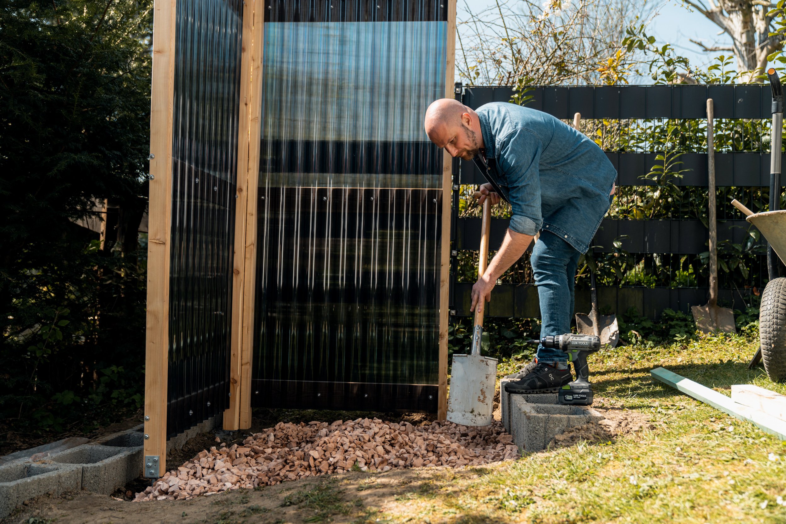 La persona distribuisce ghiaia con la pala sul fondo della doccia da giardino.