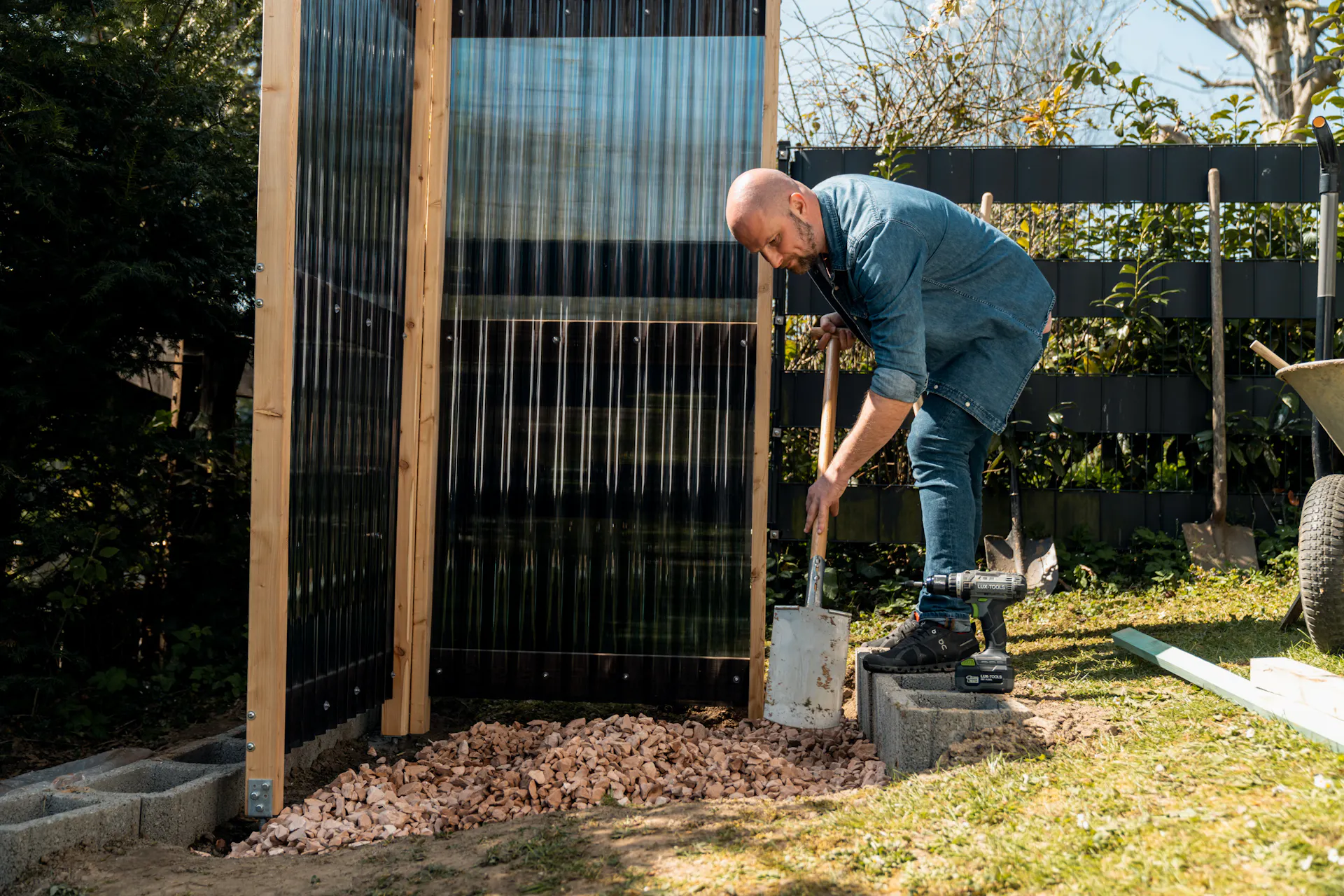 La persona distribuisce ghiaia con la pala sul fondo della doccia da giardino.