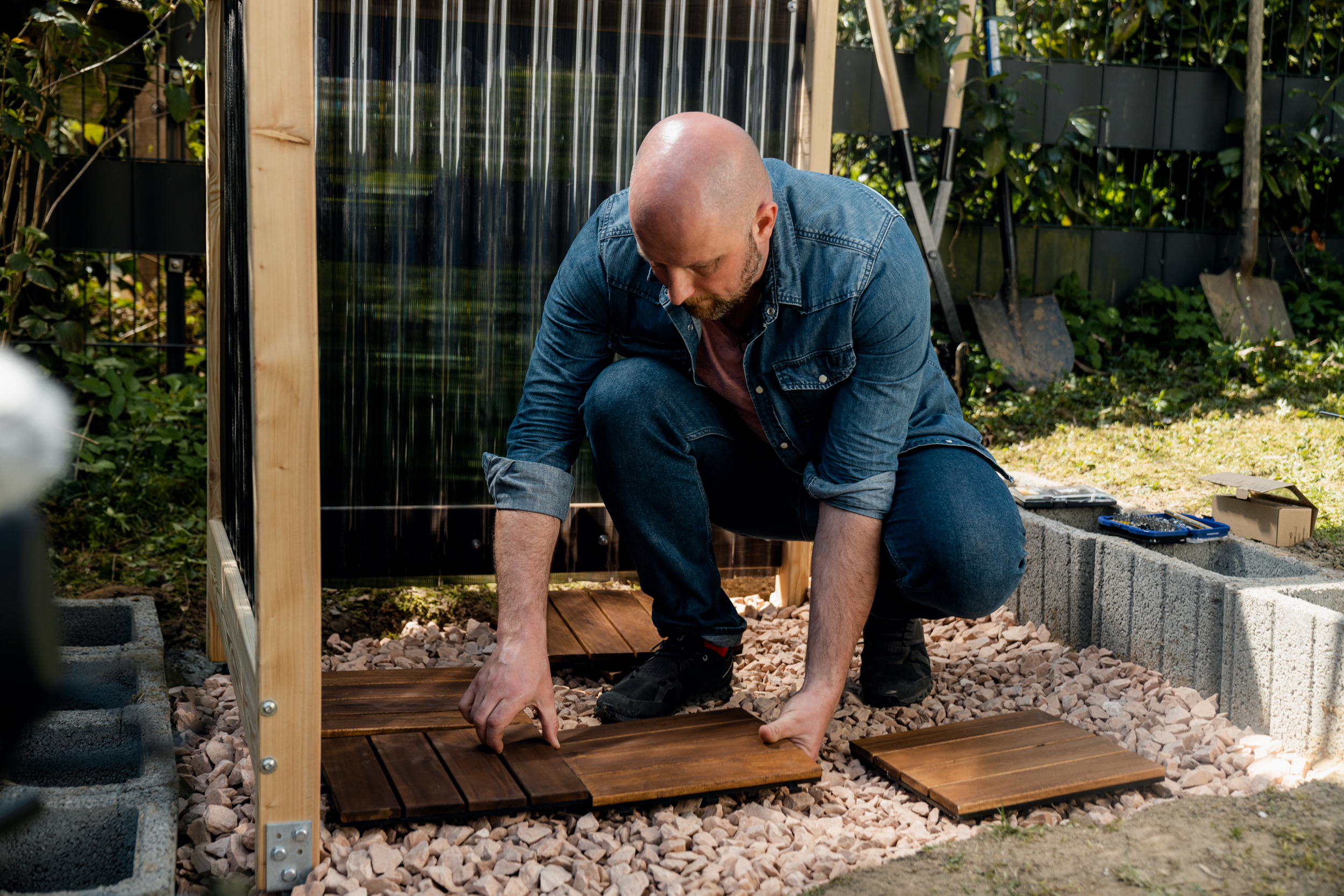 La persona posa le piastrelle a clic sulla ghiaia sul fondo della doccia da giardino.