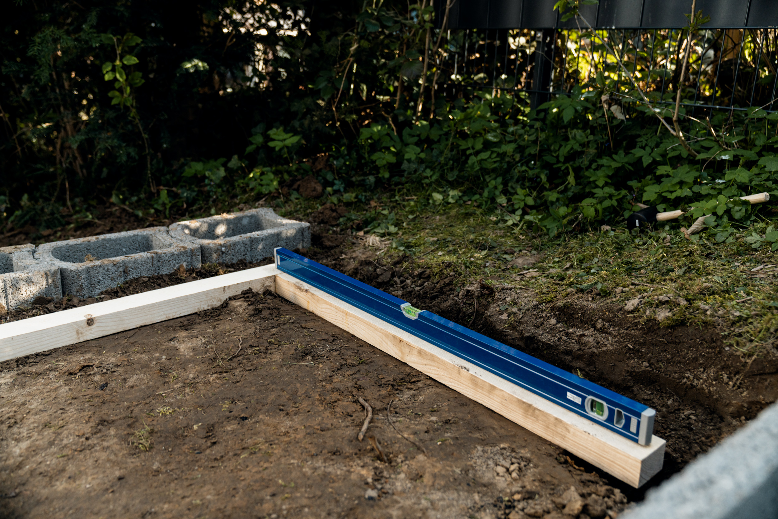 Il listello di legno con livella a bolla poggia sul terreno del giardino scavato come struttura ausiliaria per le fondamenta.