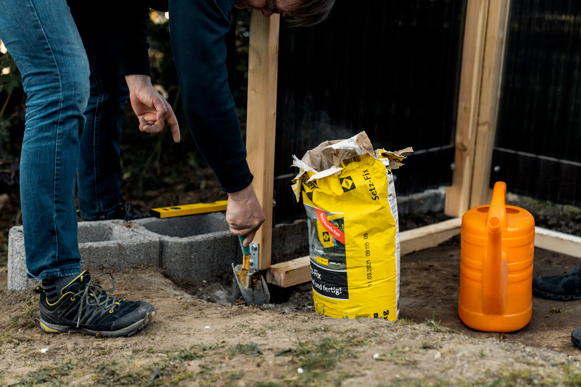L’amante del fai da te riempie le buche con calcestruzzo rapido in giardino per fissare i pali di legno.