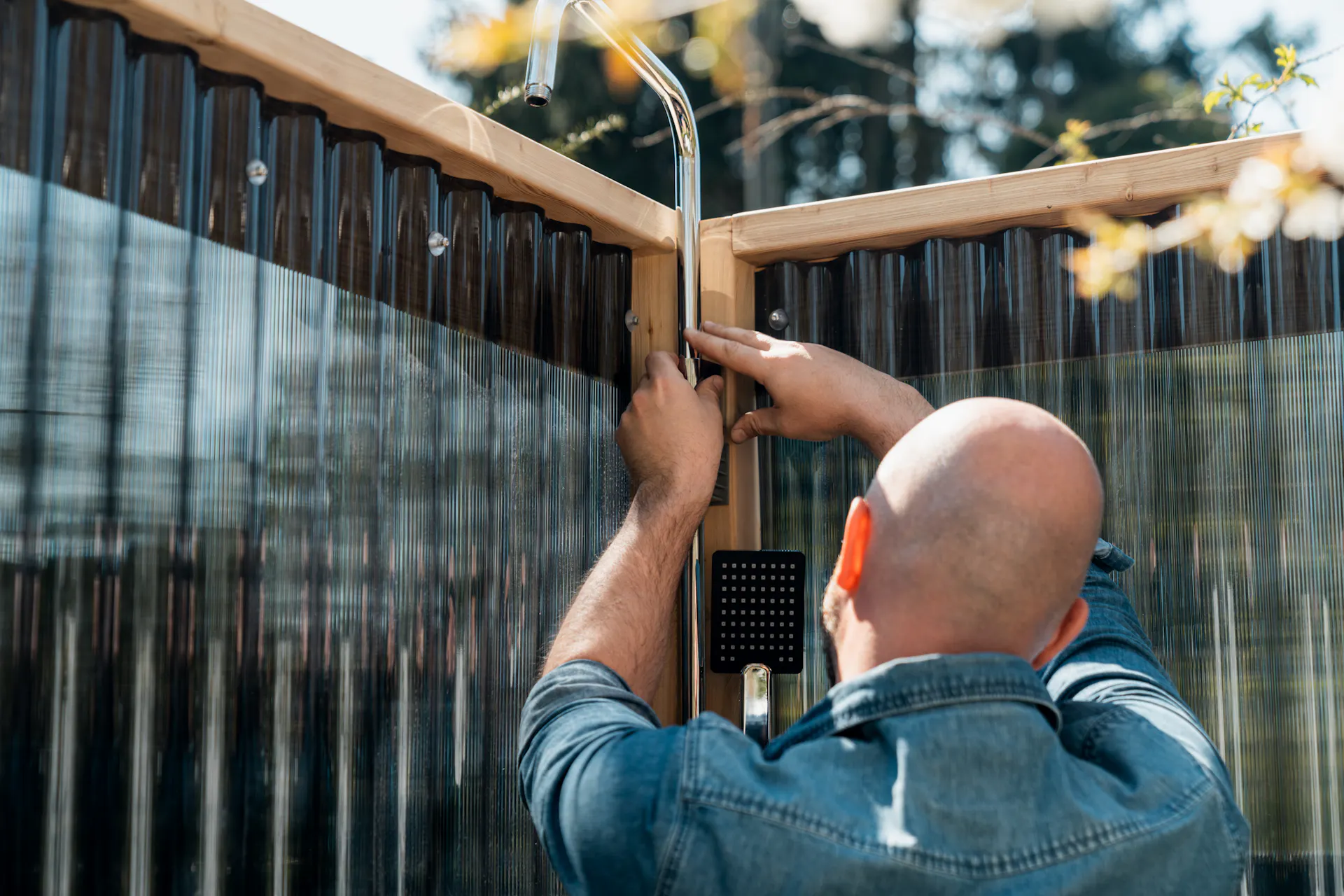 L’amante del fai da te fissa il miscelatore per doccia al listello di legno della parete della doccia da giardino.