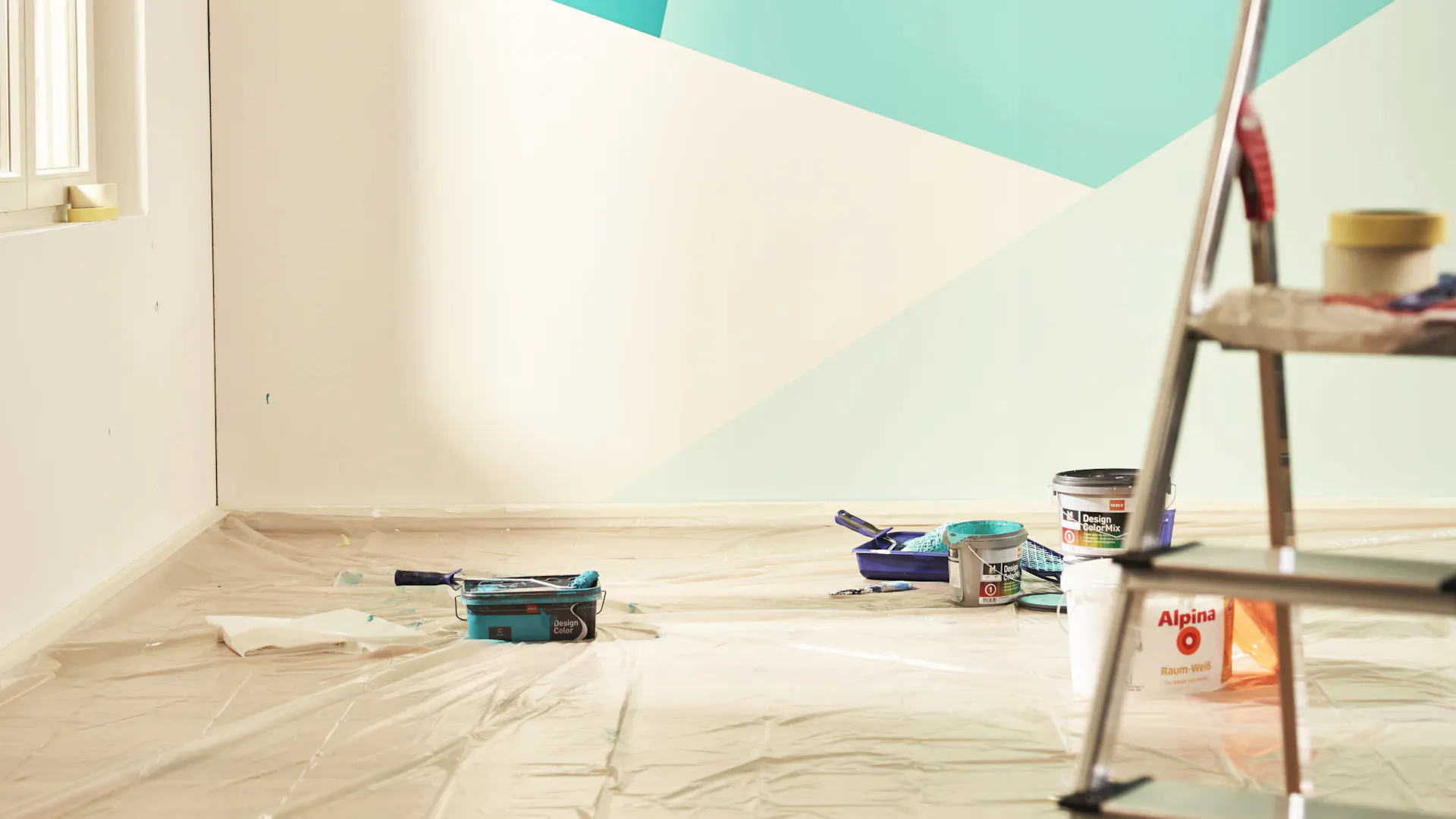 Parete verniciata in diverse tonalità di blu e motivi geometrici, pellicola protettiva e secchio per pittura sul pavimento e scala in primo piano