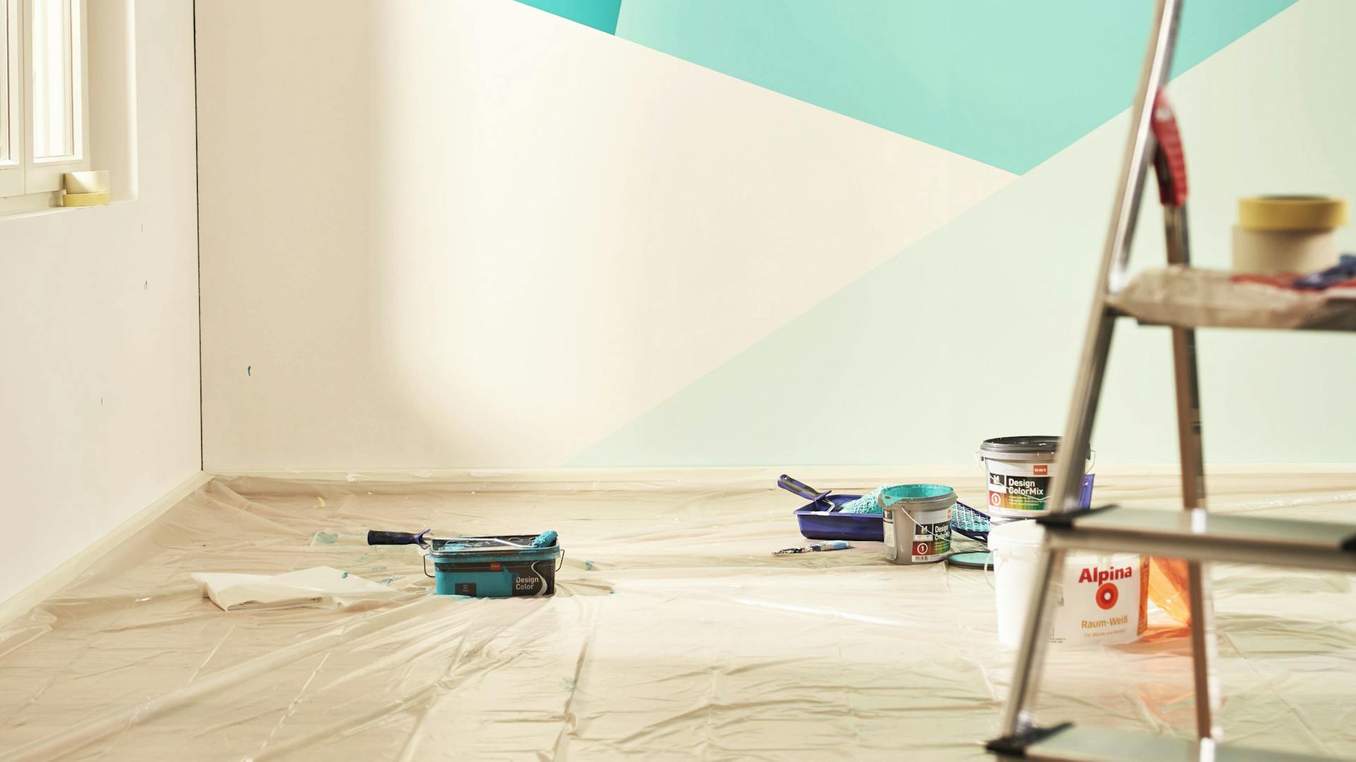 Verschiedene Malerutensilien vor einer neu gestalteten Wand mit verschiedenen Farbbereichen