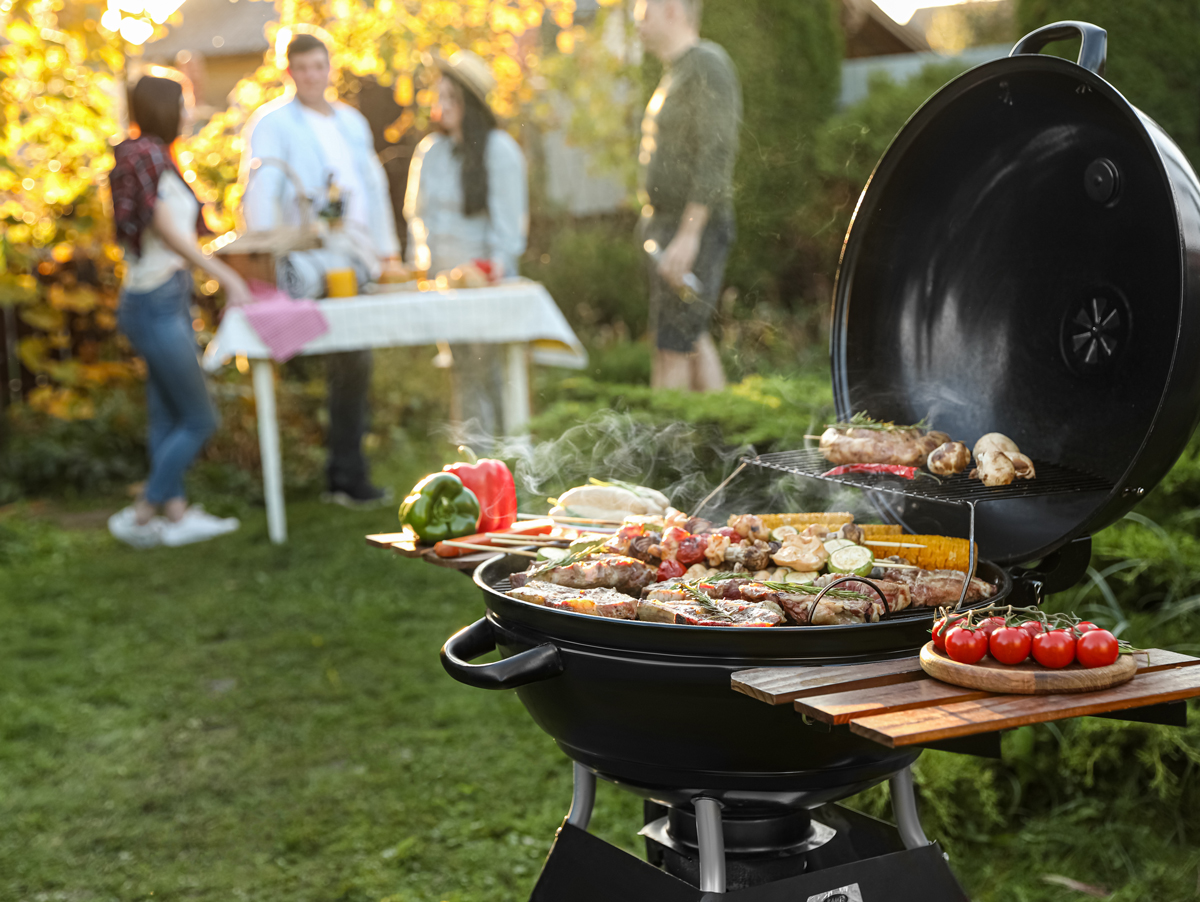 Molte persone stanno davanti a un grill a sfera con sopra gli alimenti da grigliare.