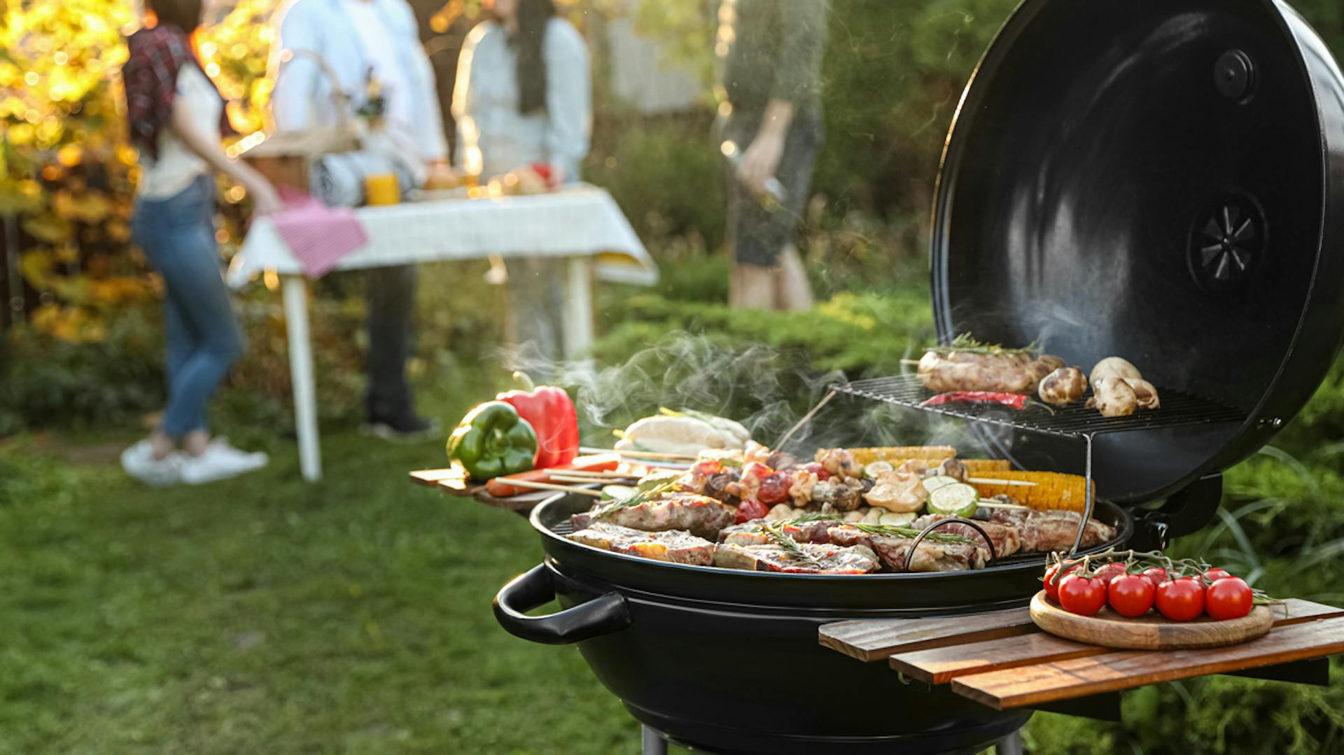 Molte persone stanno davanti a un grill a sfera con sopra gli alimenti da grigliare.