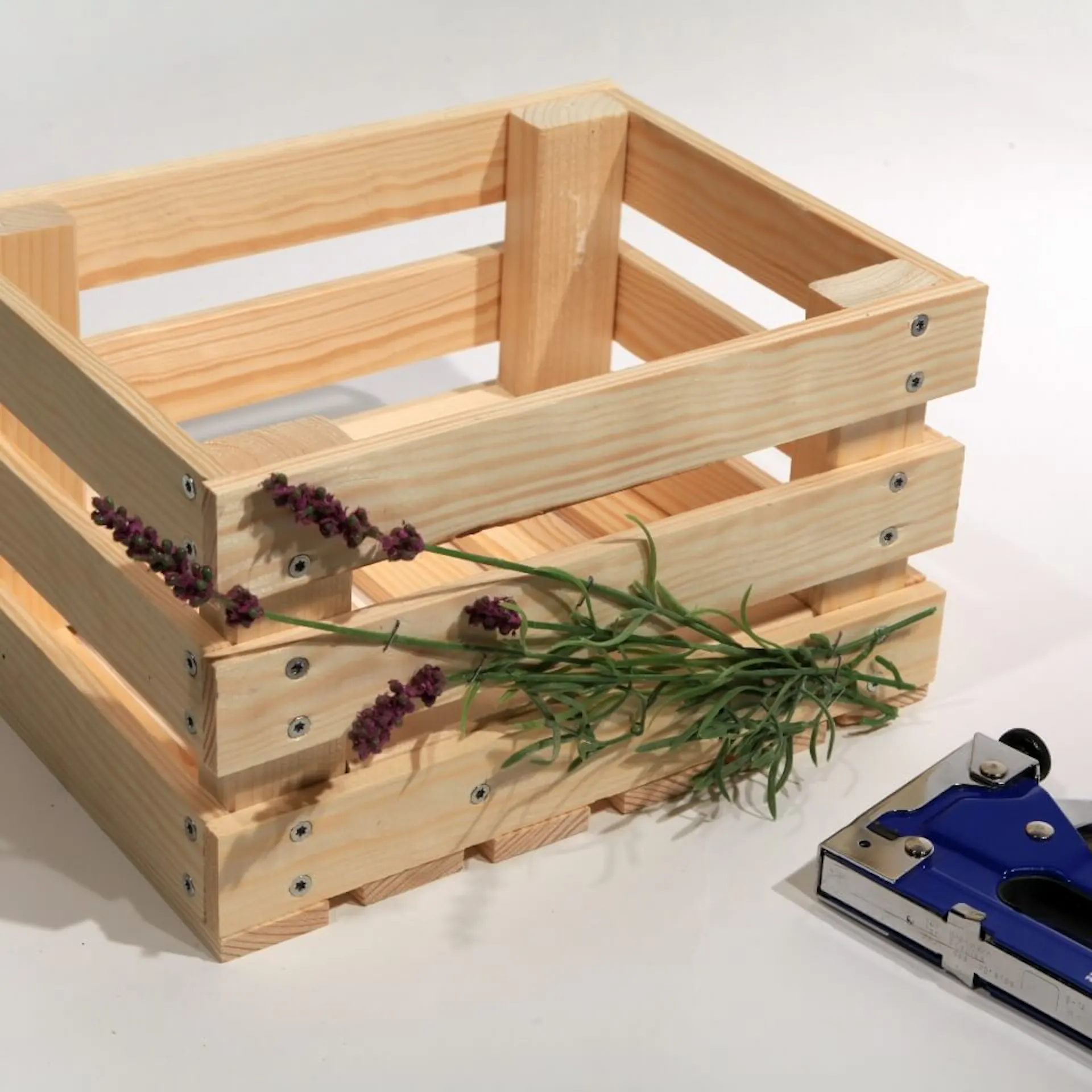 Es ist eine Holzkiste zu sehen, auf welcher Blumen angebracht sind. Davor liegt ein Tacker.