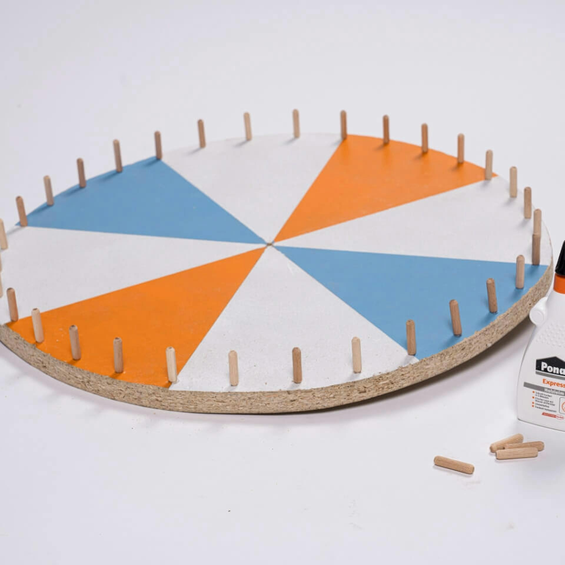 Bemaltes Glücksrad mit Dübeln am Rand neben Holzleimflasche