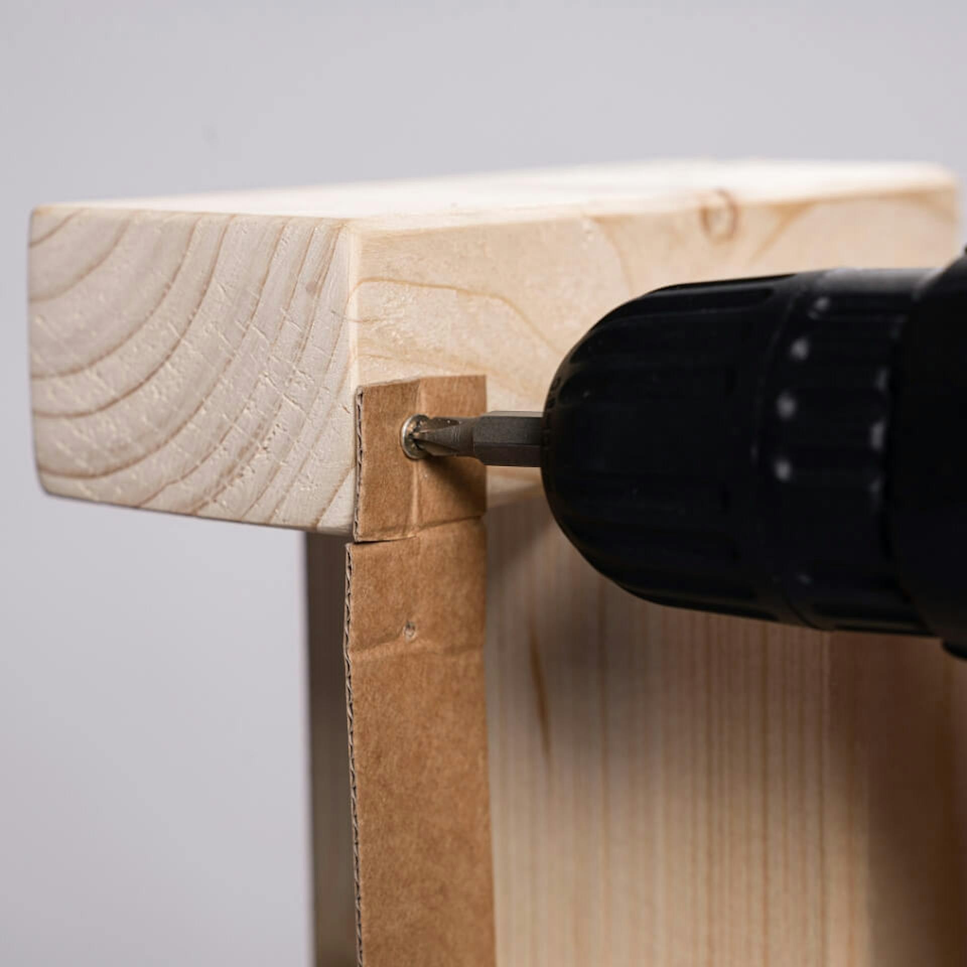 Akkuschrauber mit Bohraufsatz befestigt Pappstück an Dachlatte.