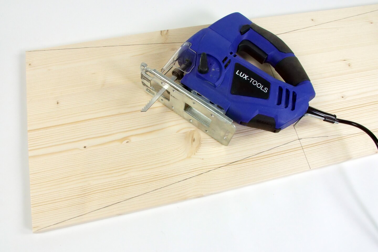 Es ist ein Holzbrett mit Bleistift-Markierungen zu sehen. Auf dem Brett liegt eine blaue Stichsäge.