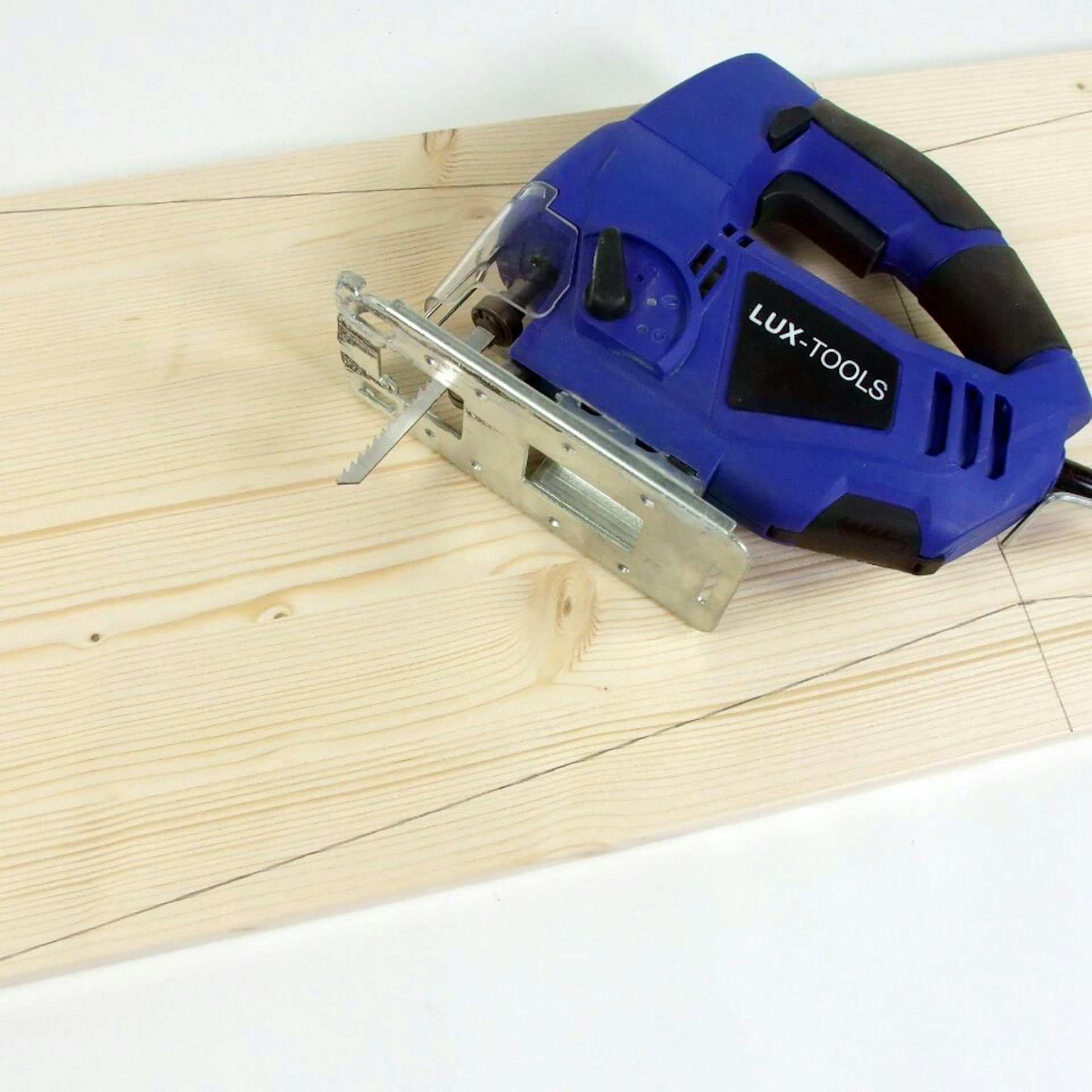 Es ist ein Holzbrett mit Bleistift-Markierungen zu sehen. Auf dem Brett liegt eine blaue Stichsäge.