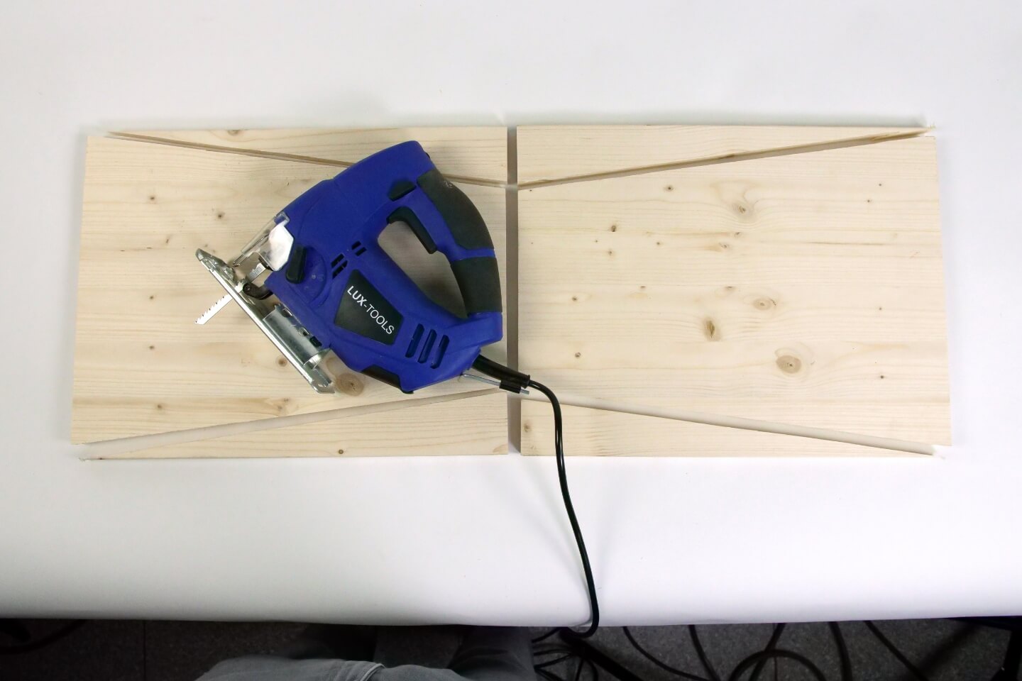 Es ist ein Holzbrett zu sehen, welches in mehrere Holzelemente zersägt wurde. Auf einem Brett liegt eine blaue Stichsäge.