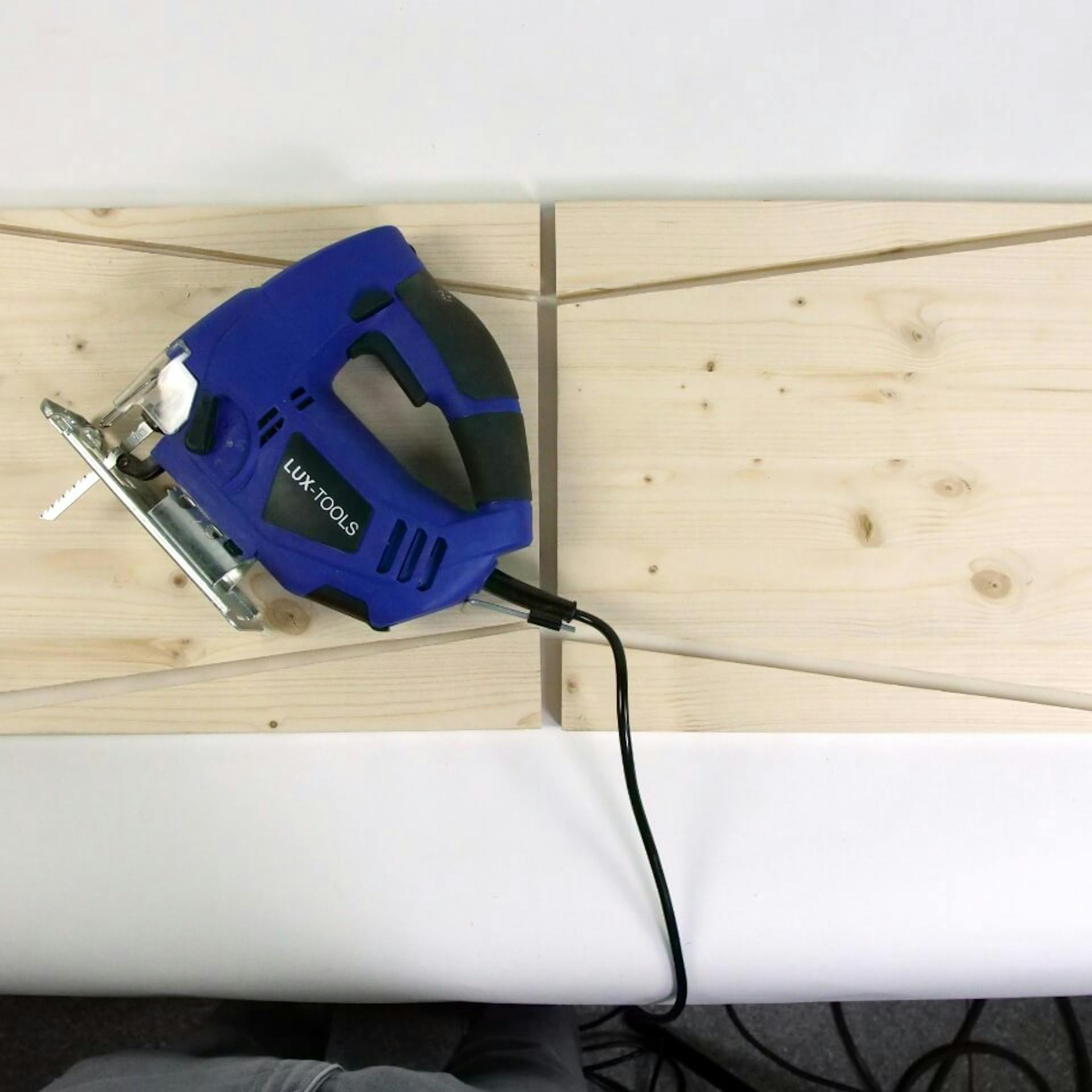 Es ist ein Holzbrett zu sehen, welches in mehrere Holzelemente zersägt wurde. Auf einem Brett liegt eine blaue Stichsäge.