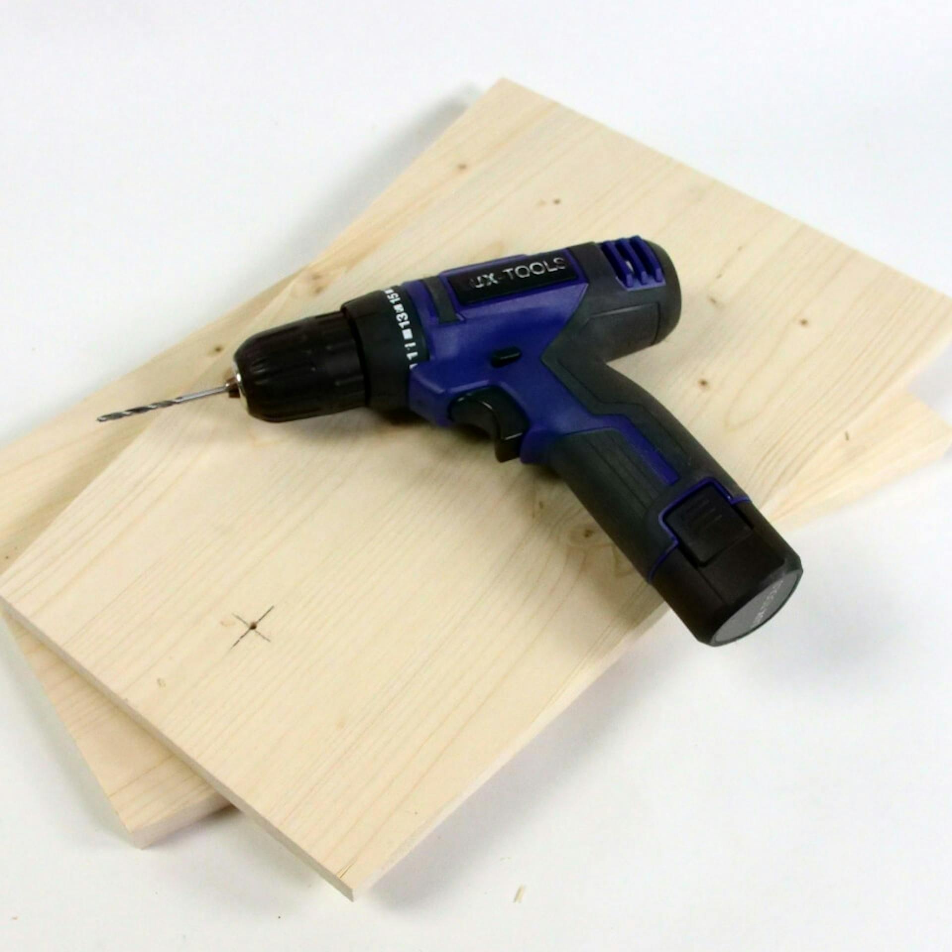 Es sind zwei aufeinander liegende Holzbretter zu sehen. Auf den Brettern liegt ein Akkuschrauber.