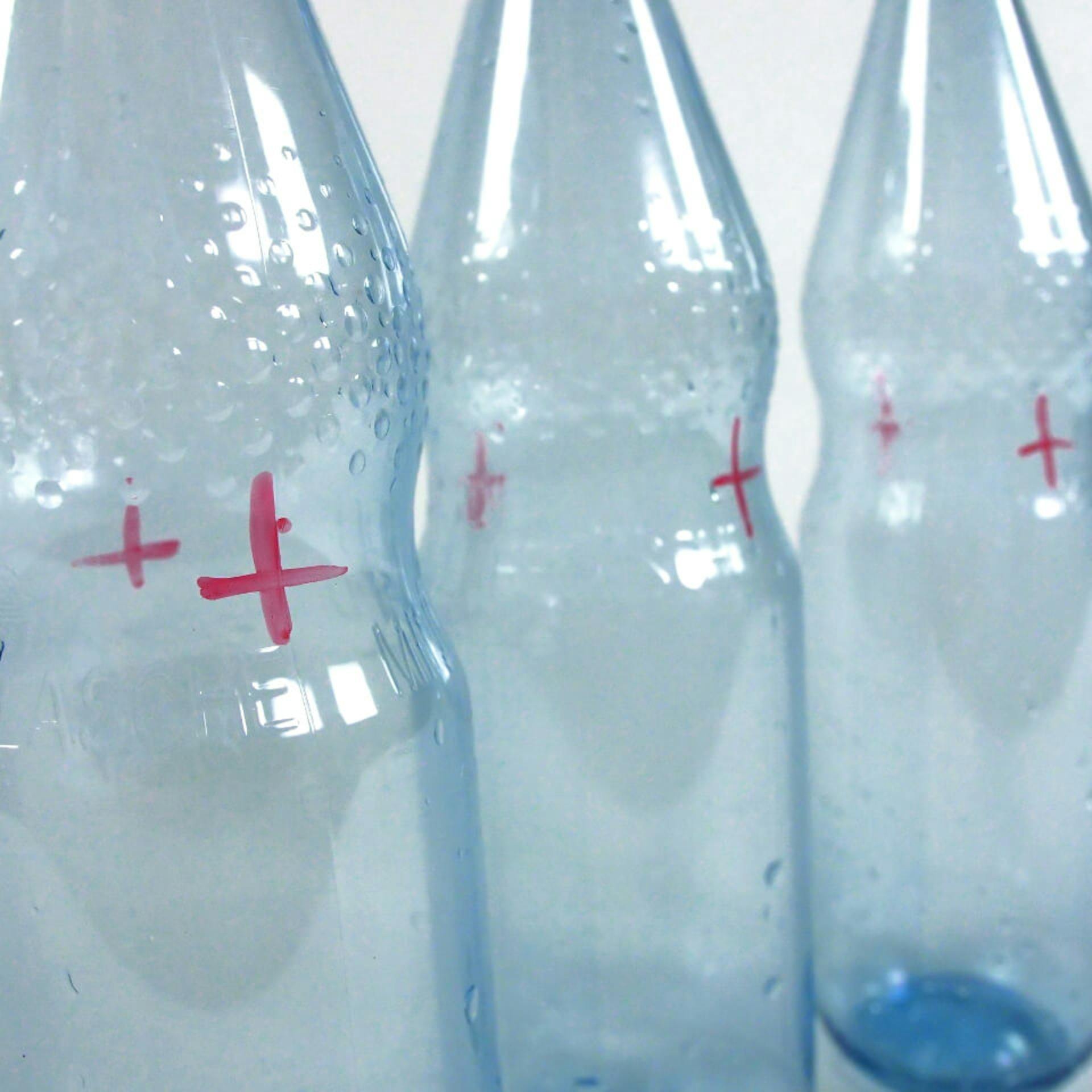 Es sind drei Plastikflaschen zu sehen. Auf den Flaschen sind jeweils zwei rote Kreuze zu sehen.