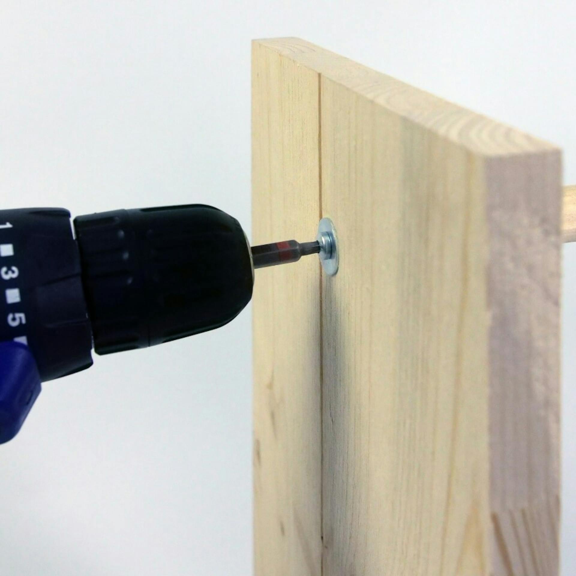 Es ist ein Akkuschrauber zu sehen, welcher ein Holzbrett und einen Rundstab aus Holz zusammenschraubt.