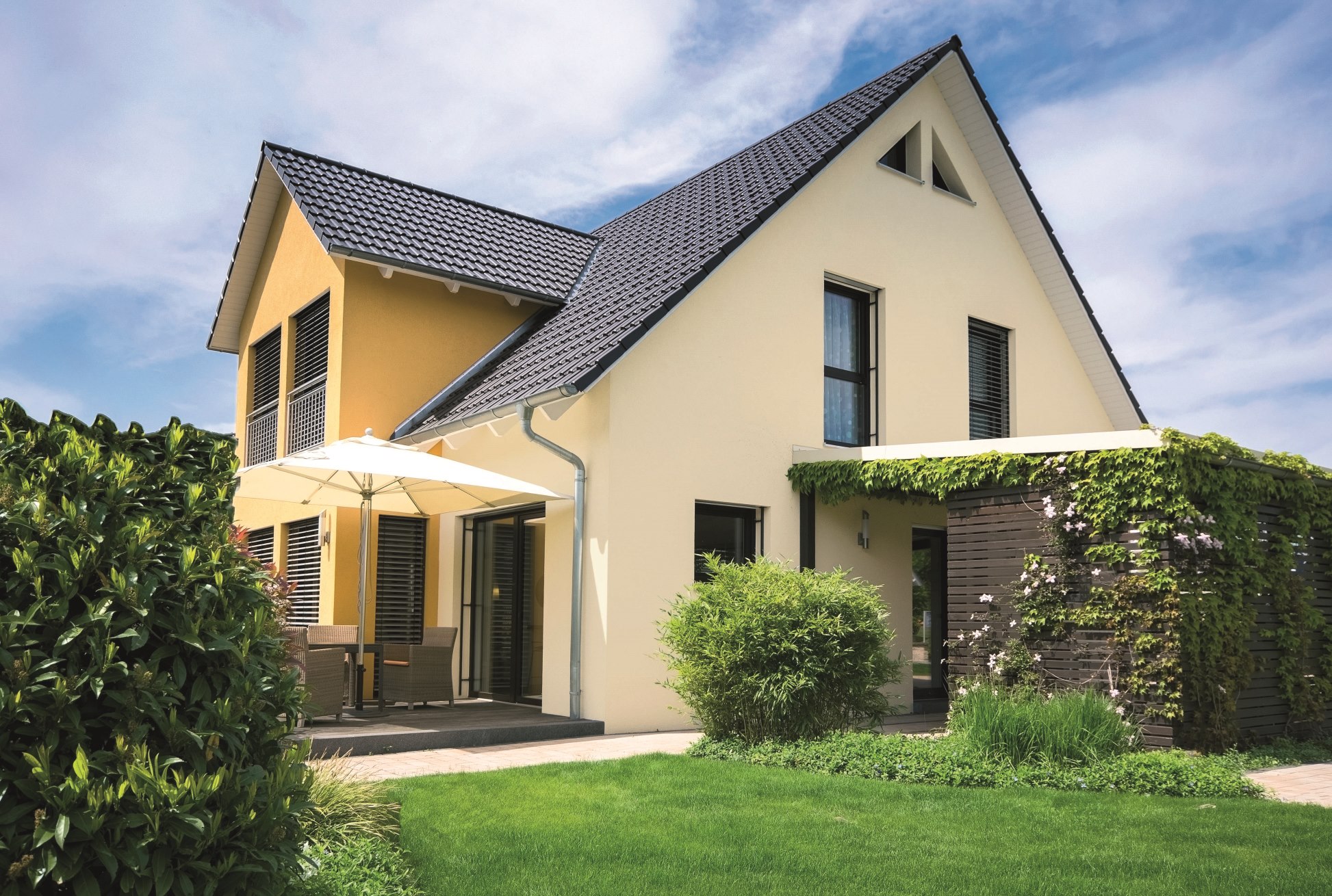 Außenansicht eines gelben, modernen Hauses mit Terrasse und Carport