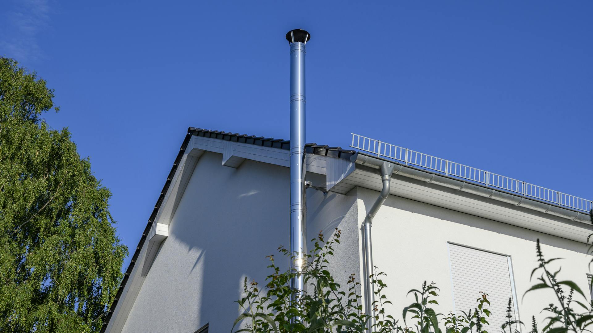 Außenschornstein aus Edelstahl an der Außenwand eines weißen Hauses.