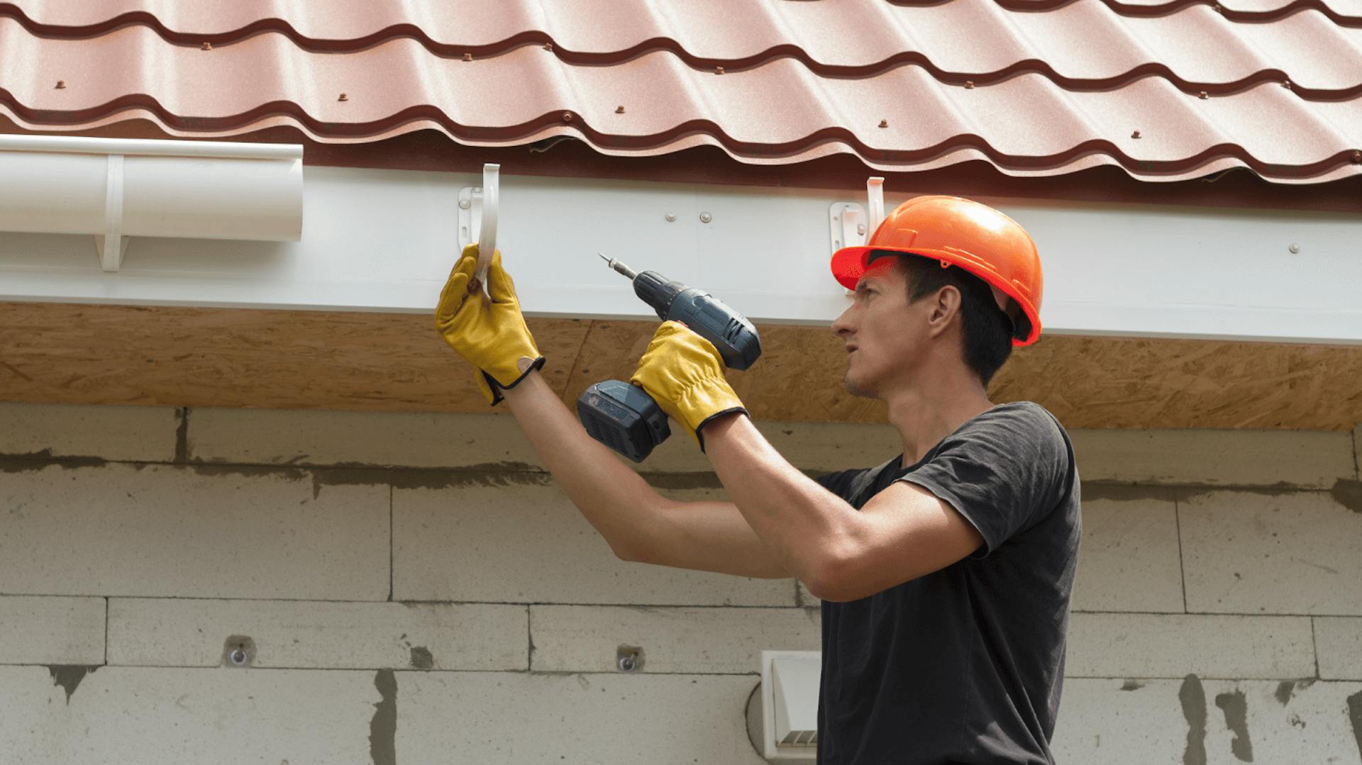 Ein Mann bringt eine Dachrinne am Haus an.