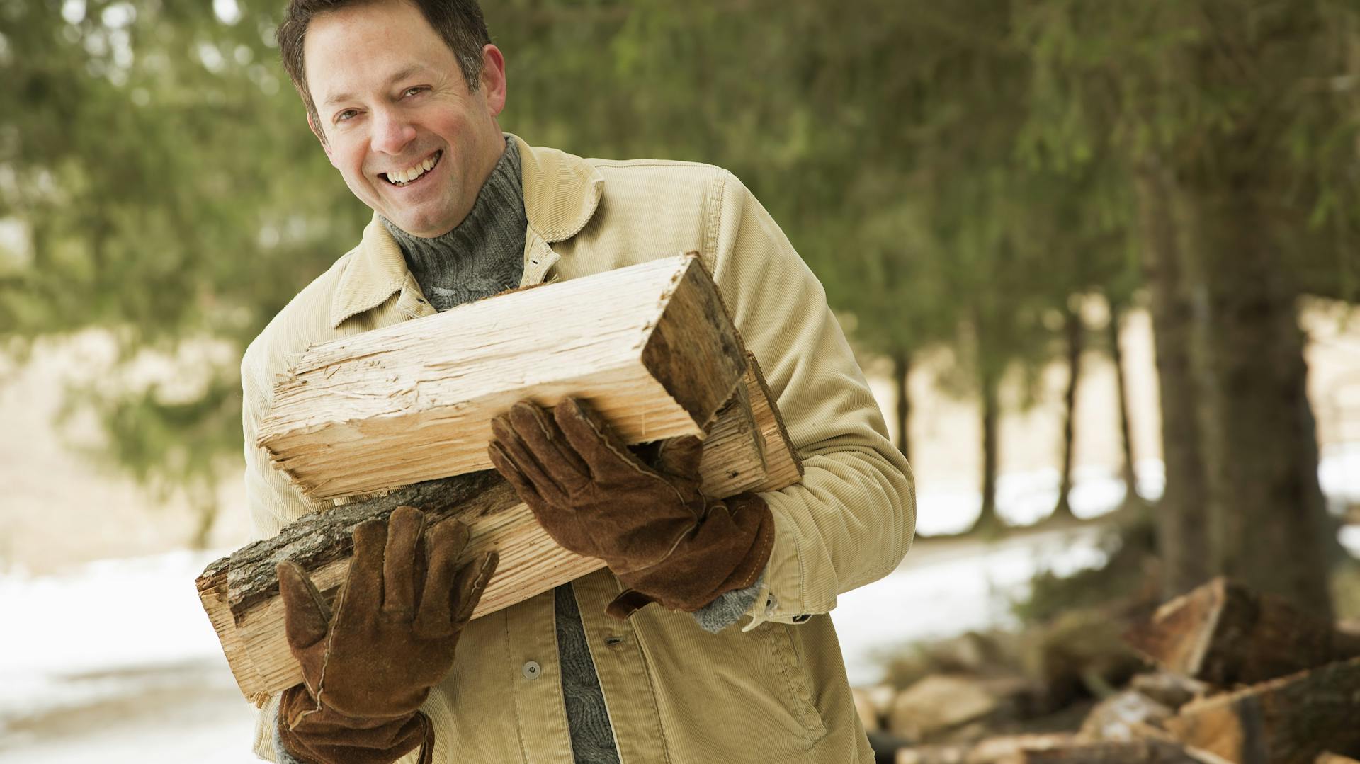 Ein Mann trägt einige Holzscheite auf dem Arm.