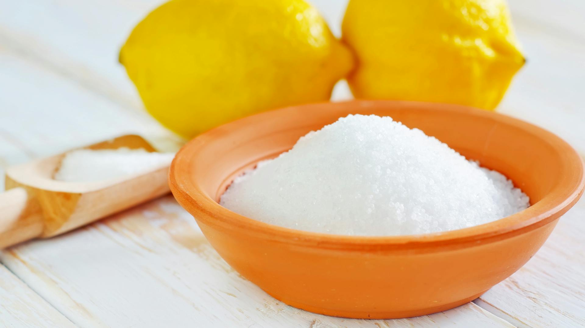 Zitronensäure in einer Schale vor zwei Zitronen.