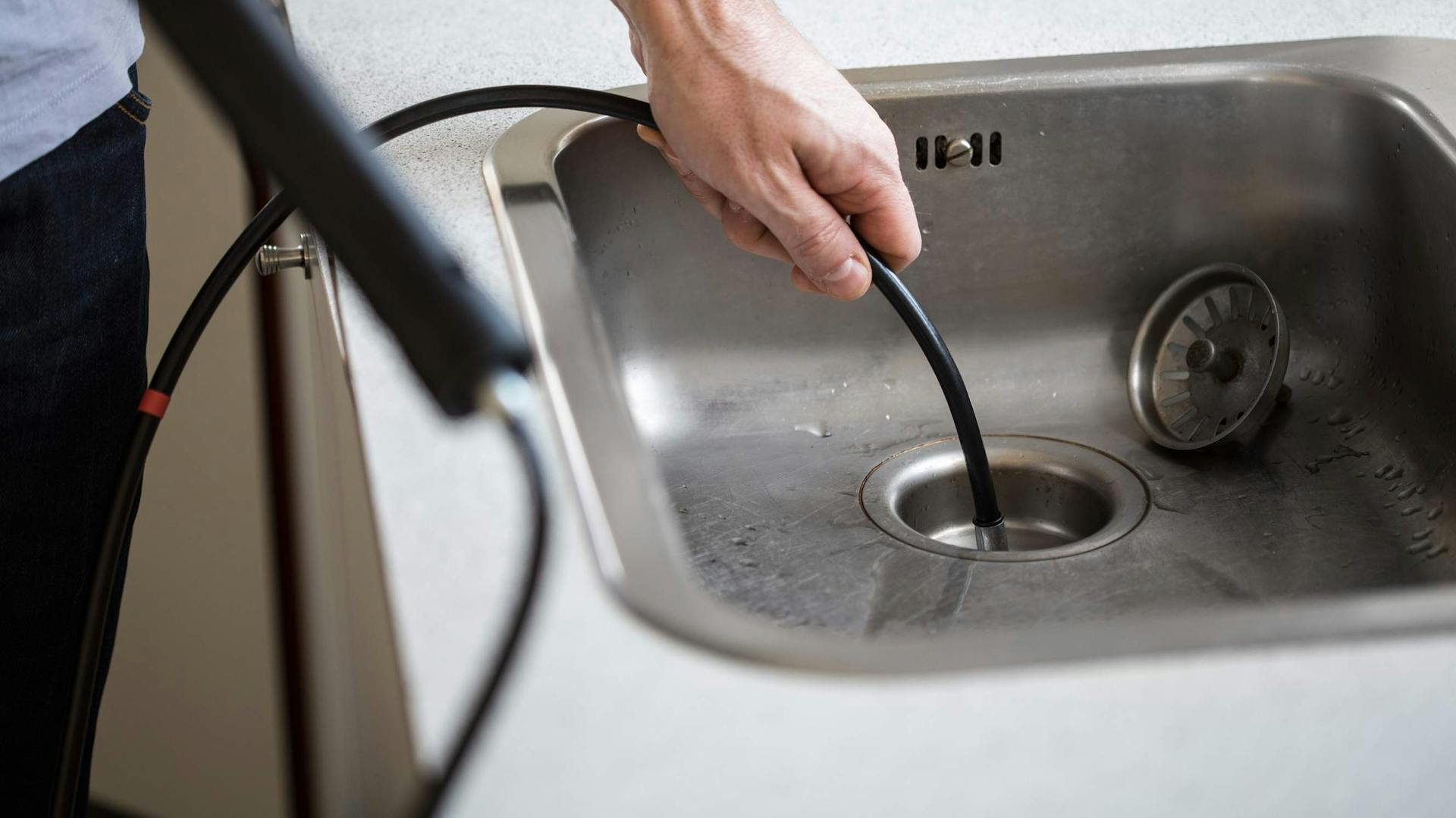Eine Person reinigt einen Abfluss in der Küche mit einer Spirale
