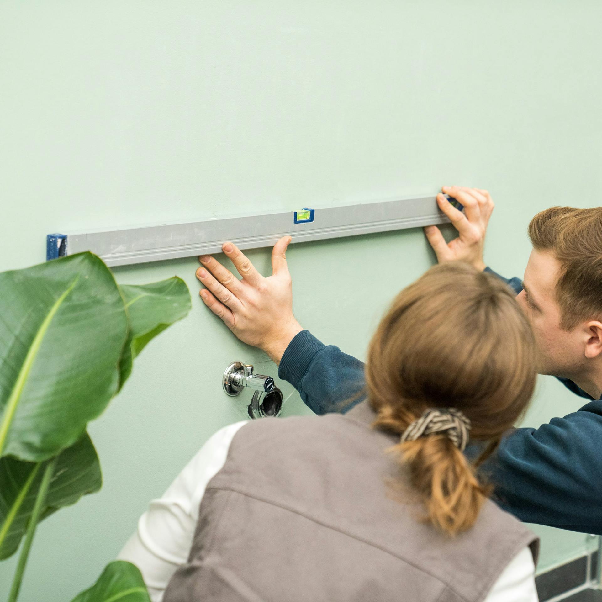 Heimwerker markieren die Abstände für Wandträger eines Aufsatzwaschbeckens.