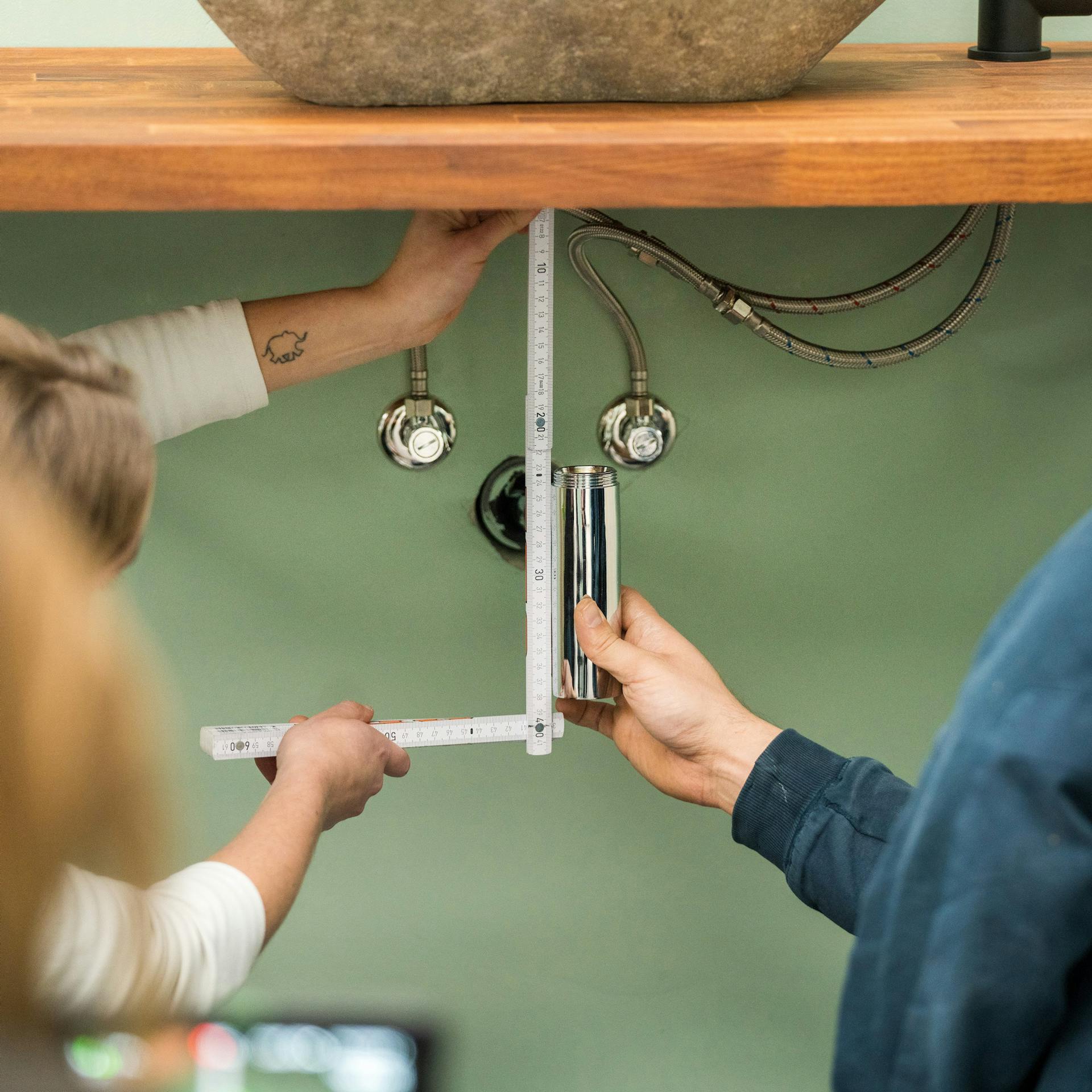 Heimwerker messen den Abstand von der Waschtische Platte zum Ablauf aus.