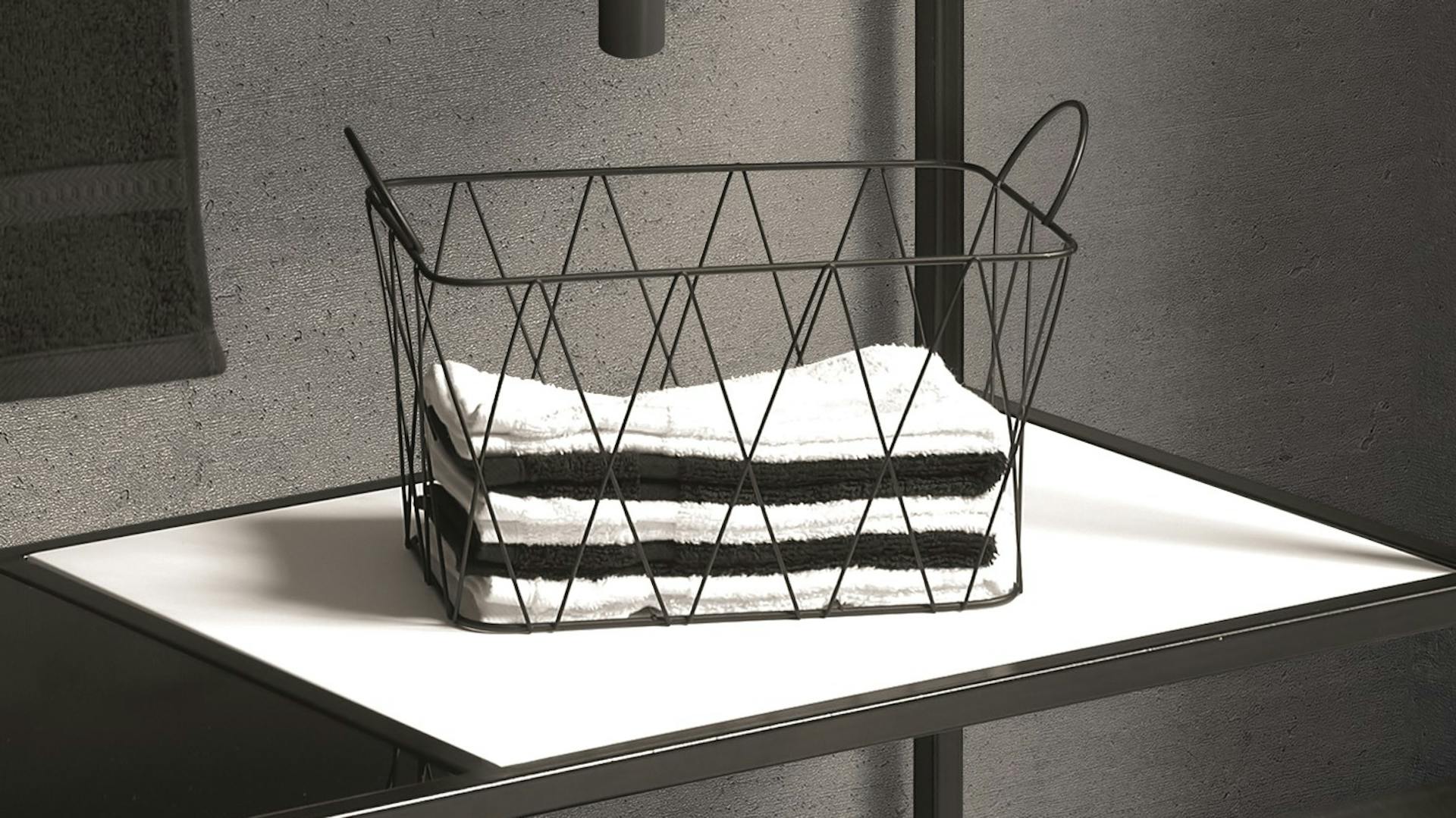 Korb aus dunkelgrauem Metall mit Handtüchern in Badezimmer in Betonoptik