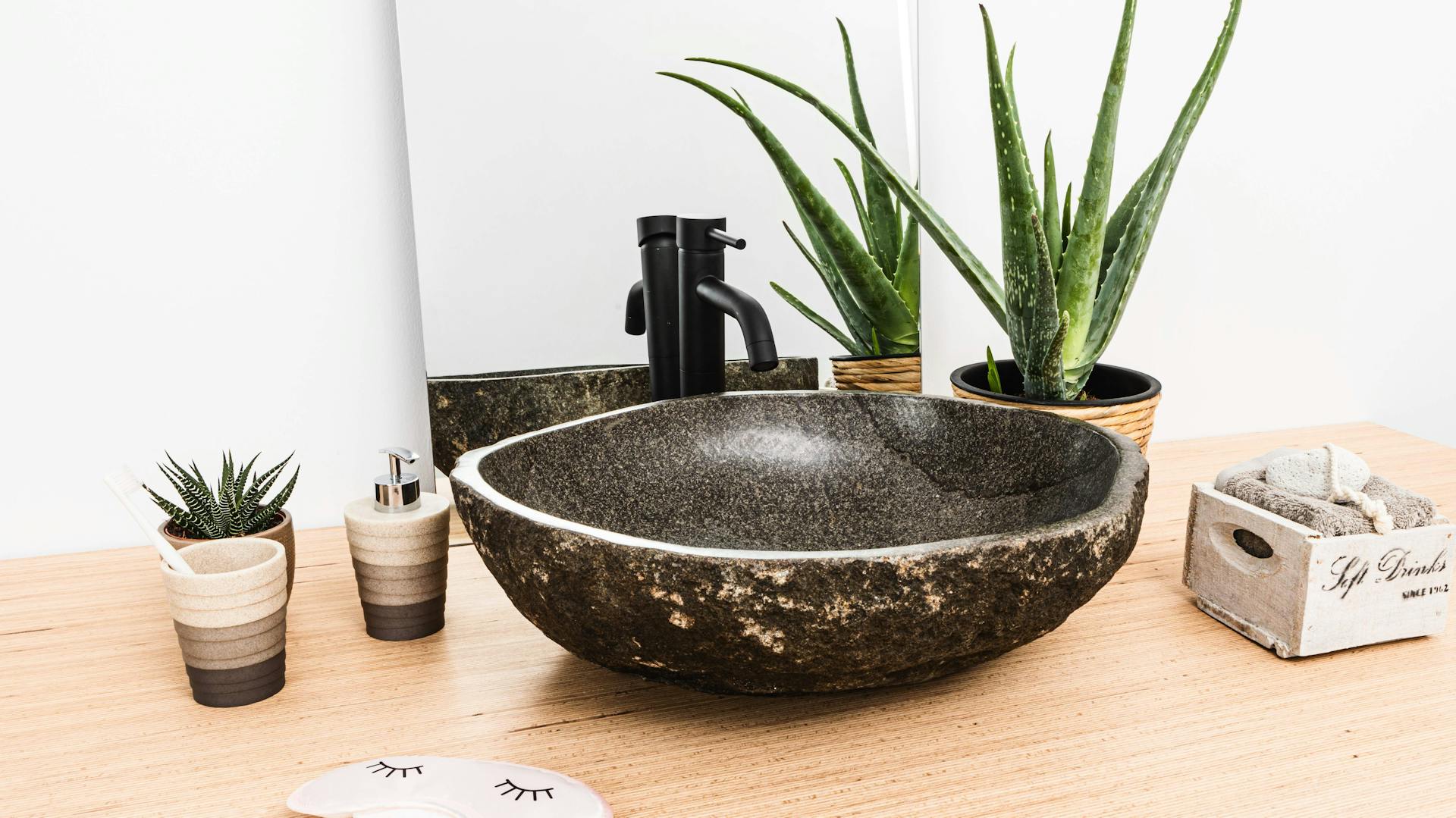 Waschbecken aus Stein auf Holzarmatur umgeben von Pflanzen.