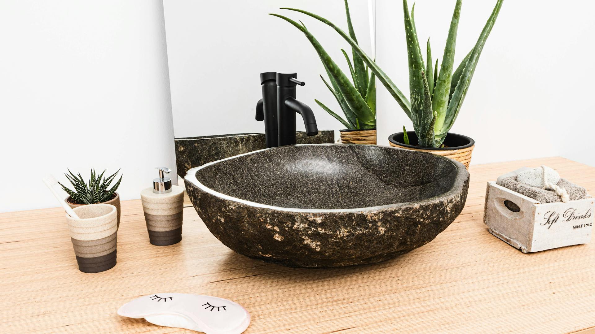 Waschbecken aus Stein auf Holzarmatur umgeben von Pflanzen.