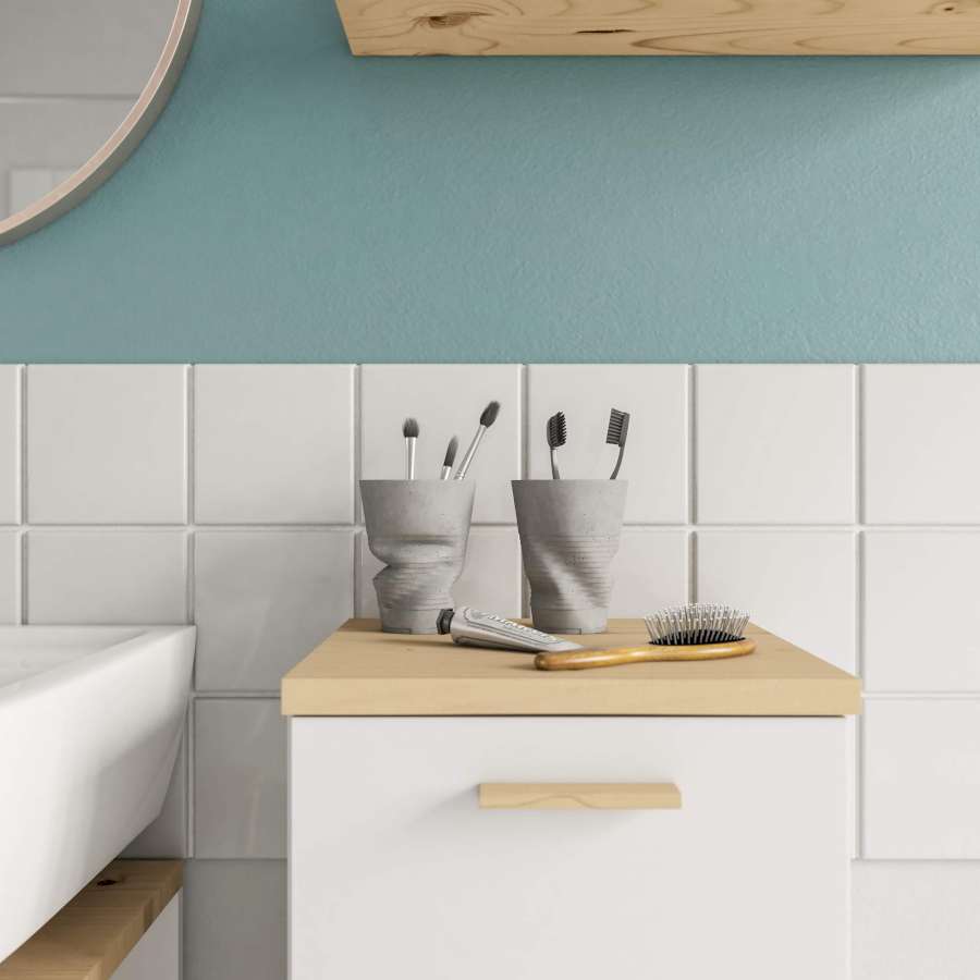 Zwei Zahnputzbecher aus Beton hinter einer Haarbürste und Handcreme auf einem Badezimmerregal