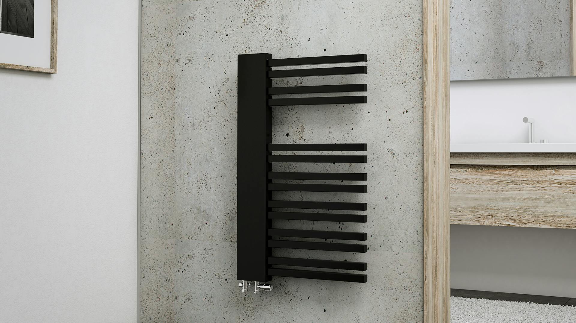 Ein schwarzer Handtuch- Heizkörper an einer grauen Wand im Badezimmer.