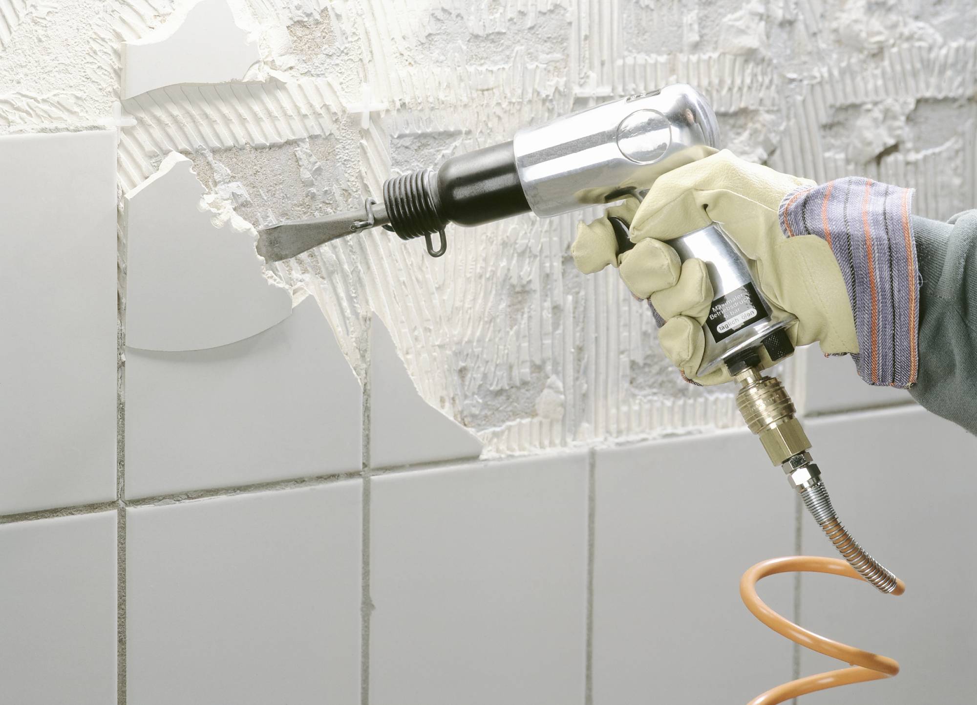 Un appassionato di fai-da-te rimuove vecchie piastrelle dalla parete con un martello scalpellatore.