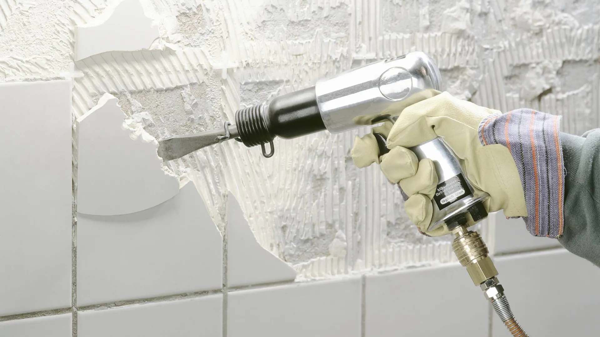 Heimwerker entfernt alte Fliesen mit einem Meißelhammer von der Wand.