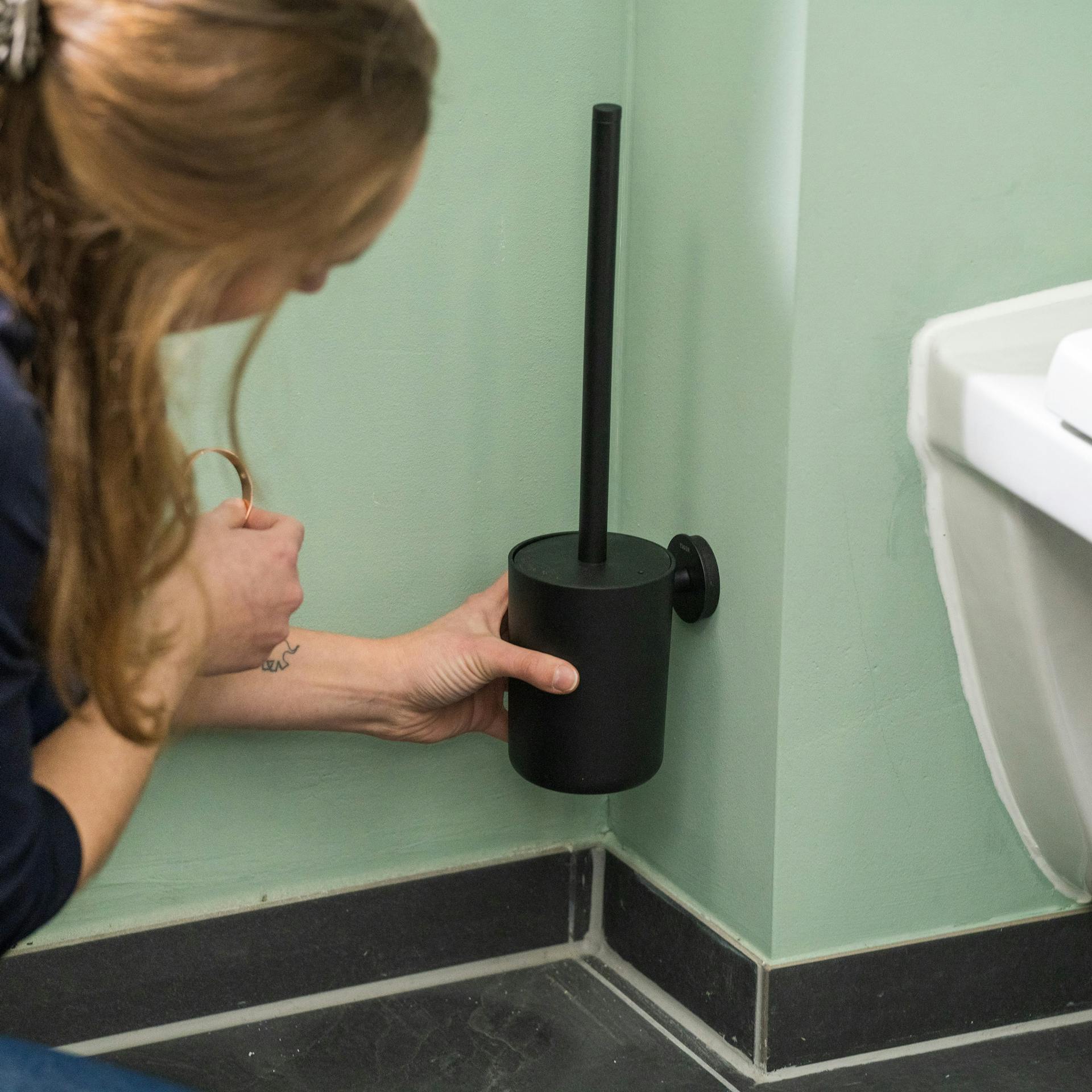 Heimwerkerin befestigt einen Klobürstenhalter an die Wand.