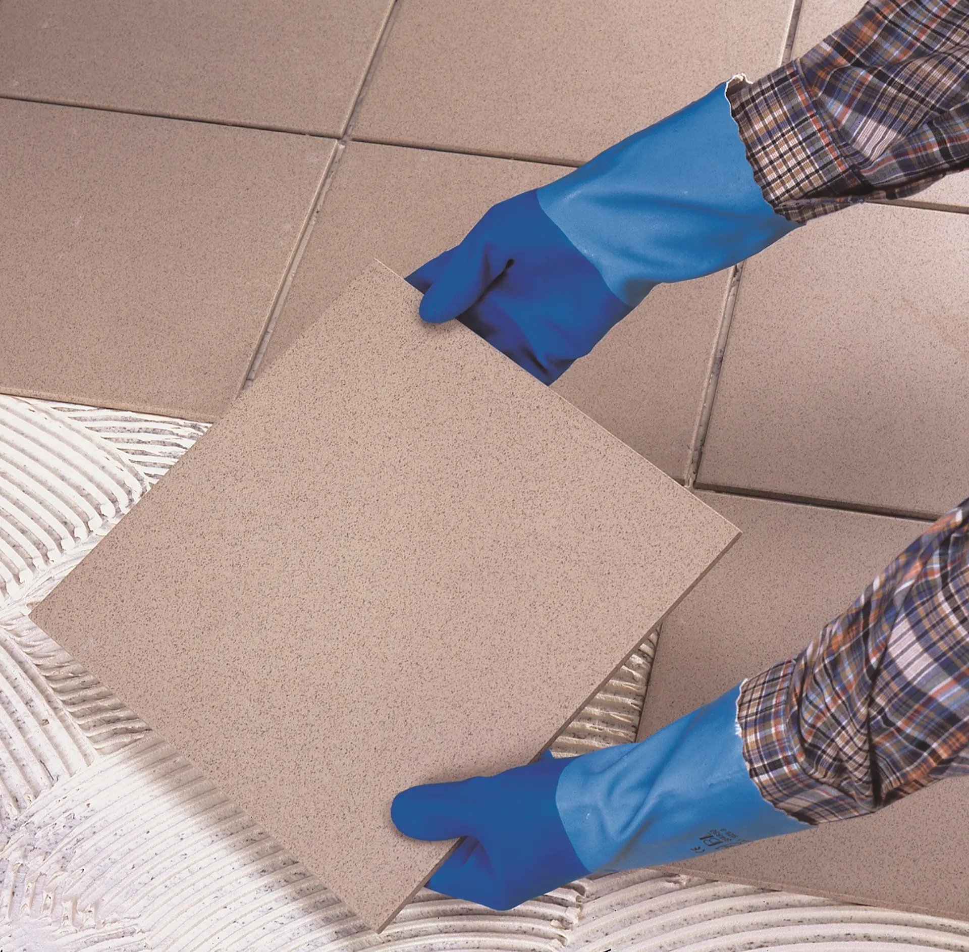 Un artisan avec des gants pose des carreaux dans une salle de bains.