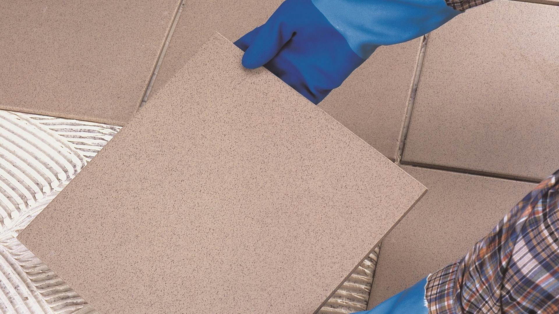 Heimwerker mit Handschuhen verlegt Fliesen im Bad.