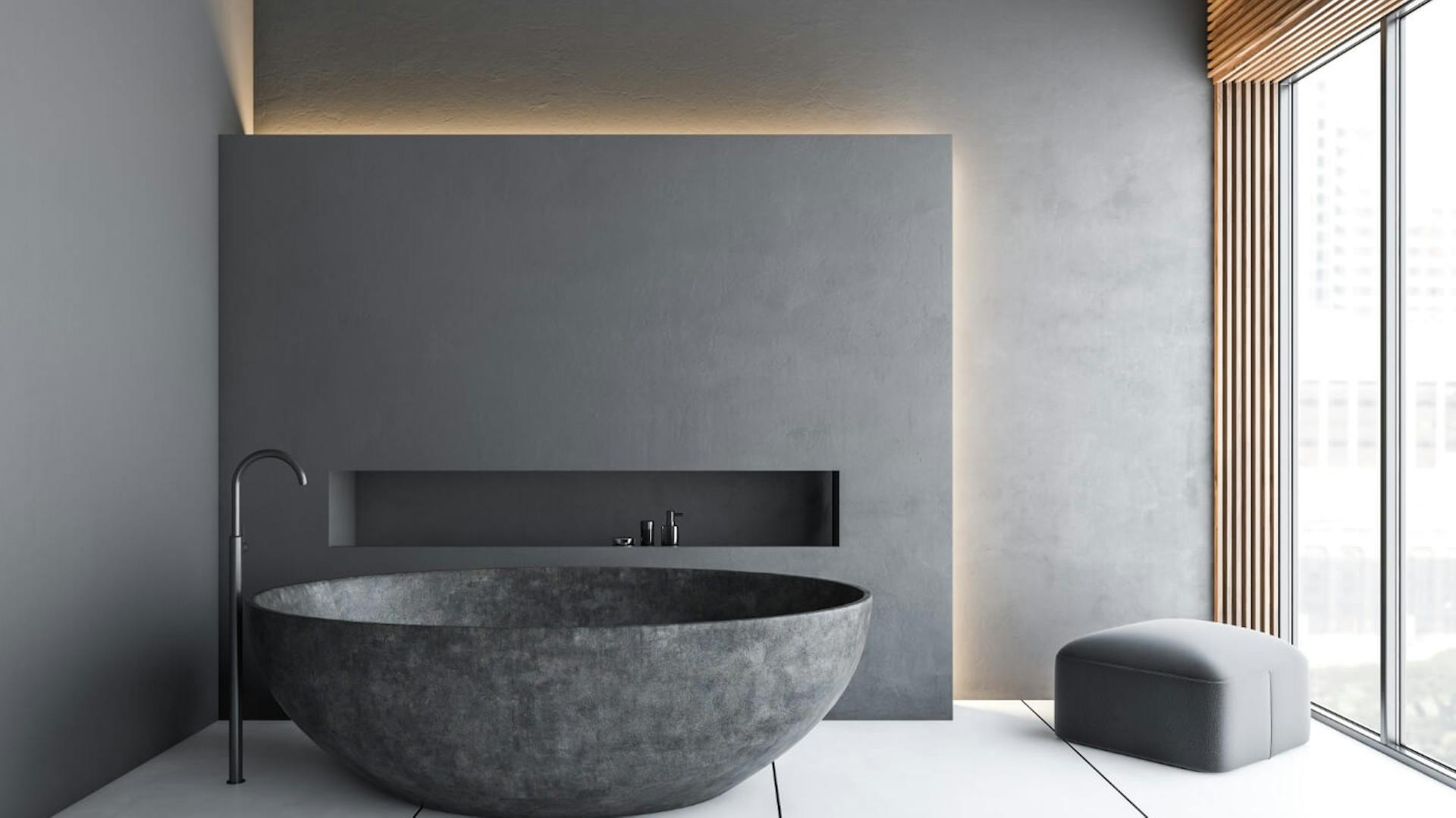 Dunkelgraue freistehende Badewanne, dahinter eine Nische mit indirekter Beleuchtung.