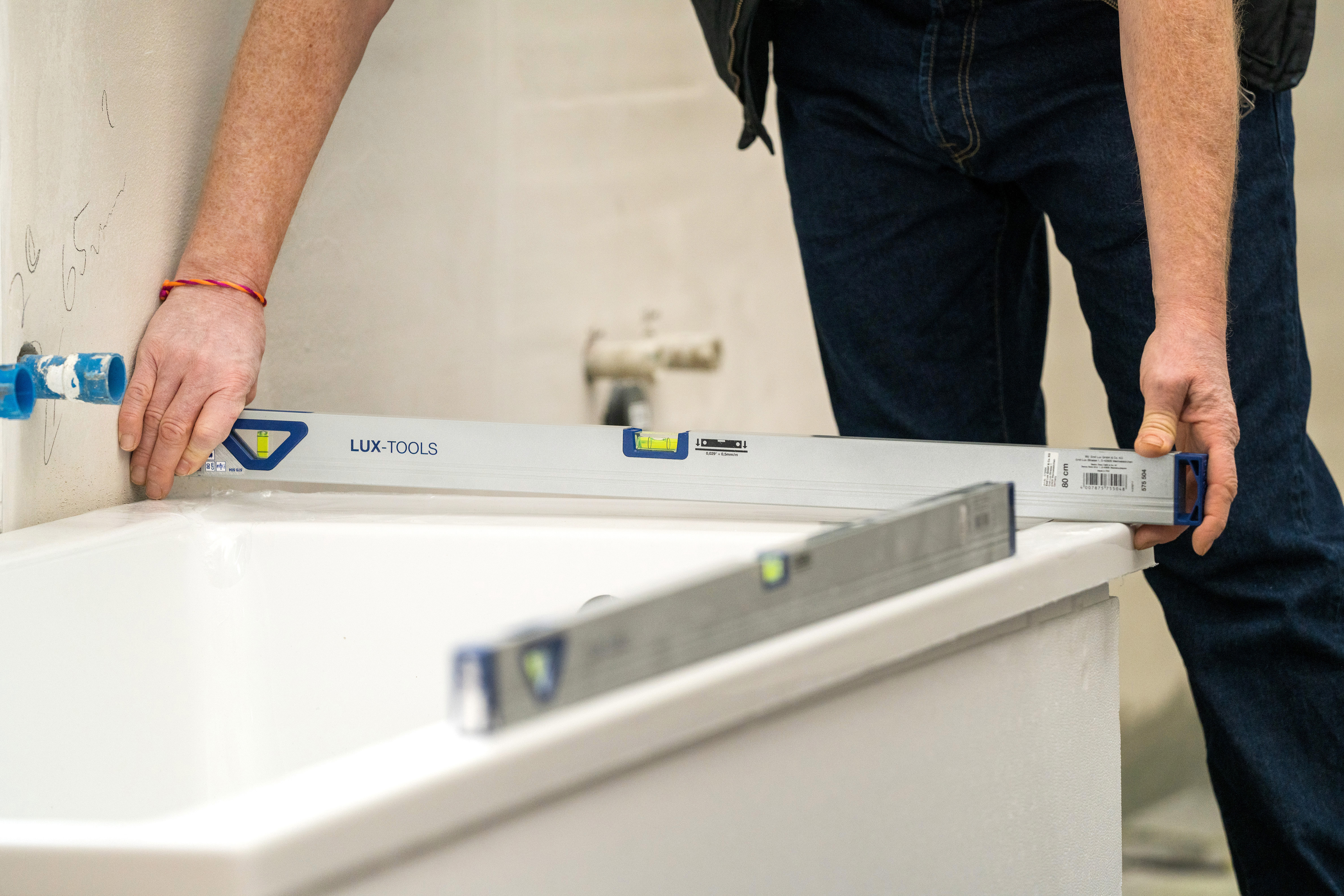 Jemand kontrolliert die Ausrichtung einer Badewanne mit einer Wasserwaage.