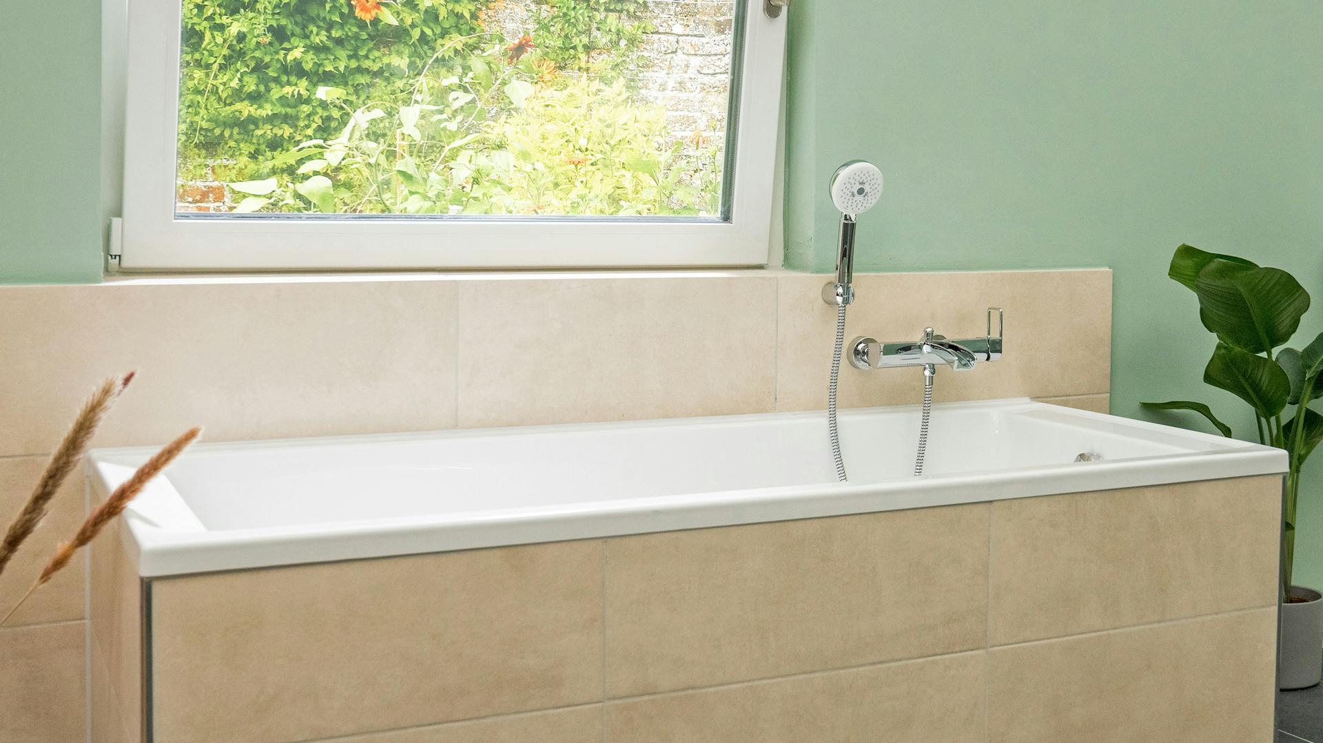 Beige gefließte Badewanne mit einer neuen, glänzenden Armatur mit Duschvorrichtung.