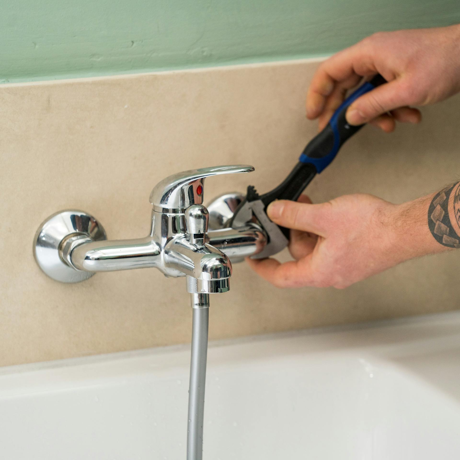 Handwerker schraubt mit Maulschlüssel eine alte Armatur ab.