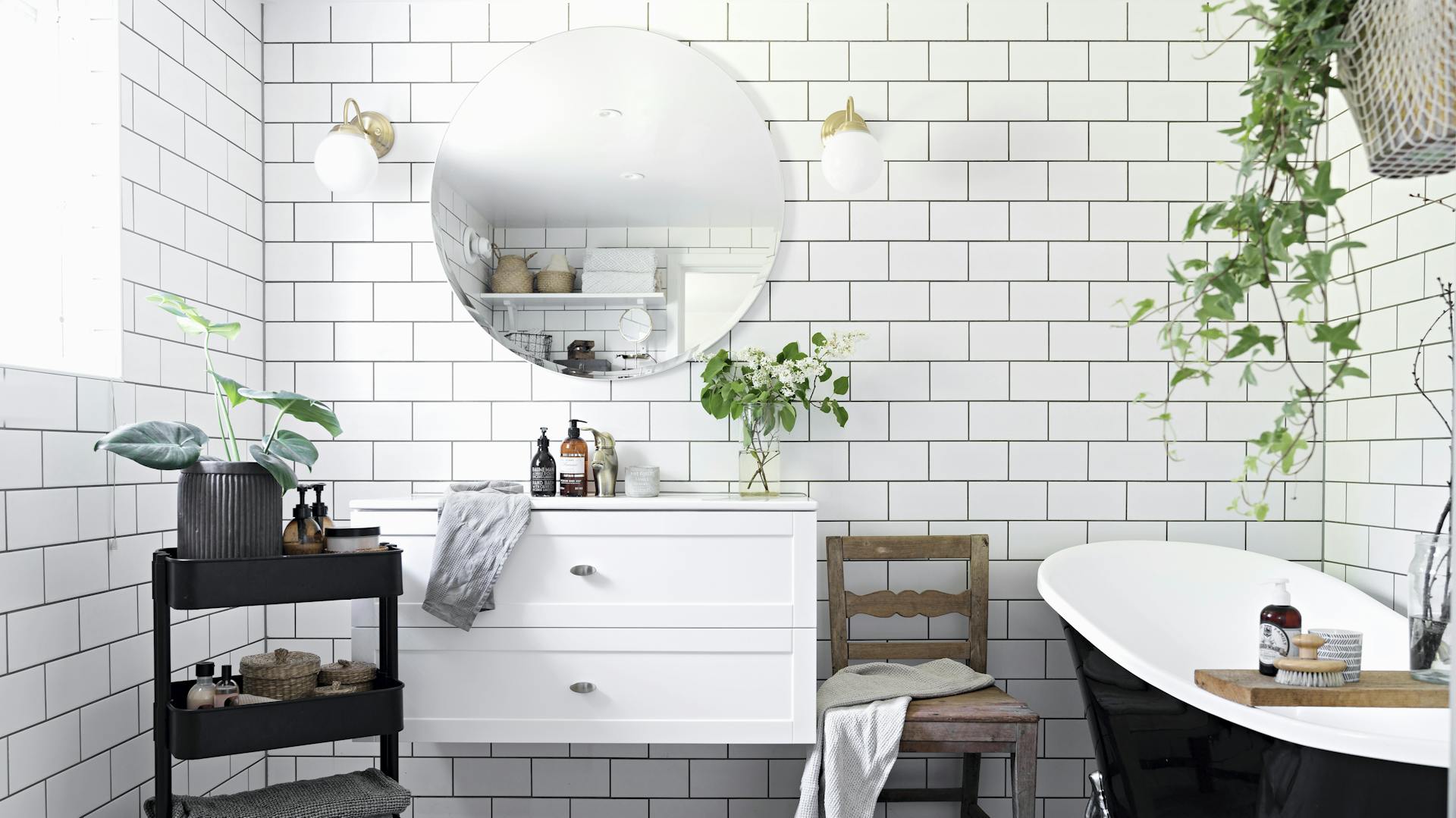 Ein weiß gefliestes Bad mit einer dunklen Badewanne und vielen Badaccessoires.