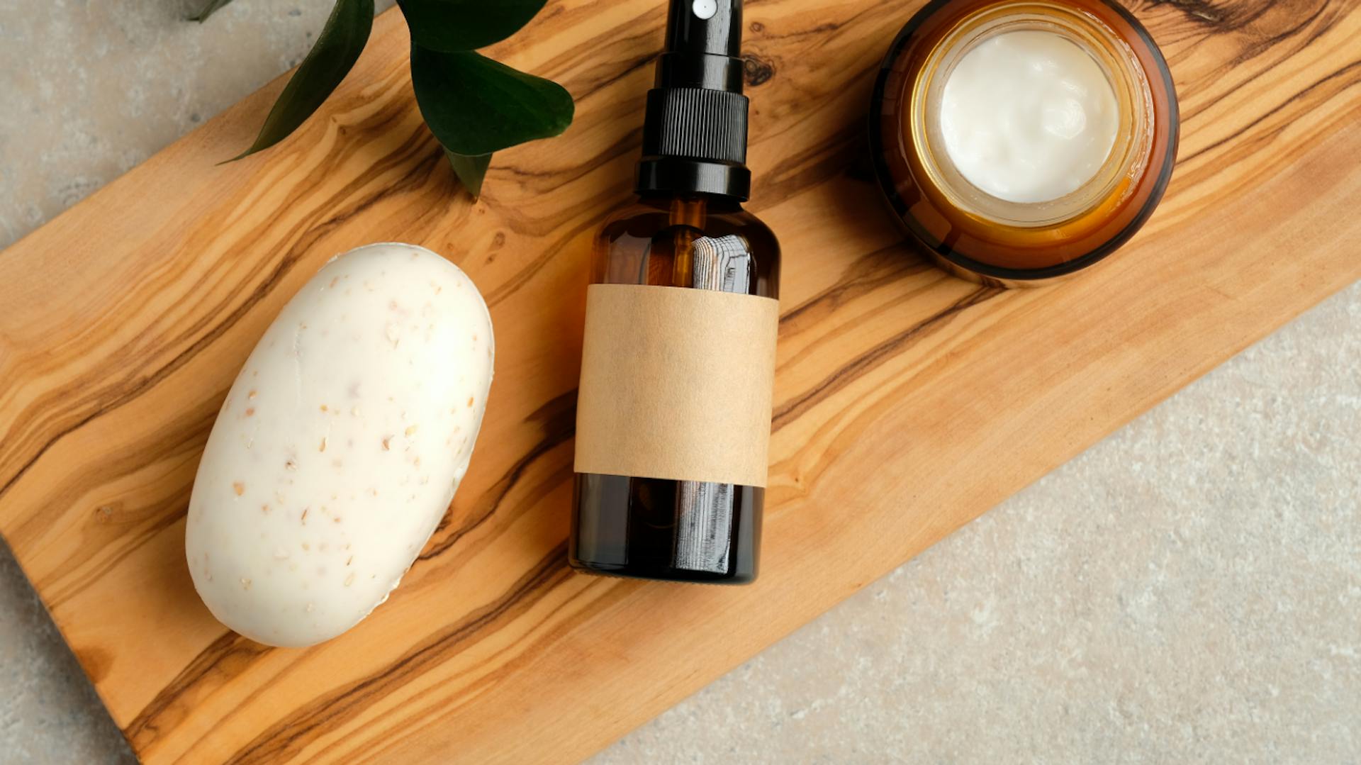 Flacone spray marrone scuro, sapone bianco e recipiente con crema su tavola di legno.