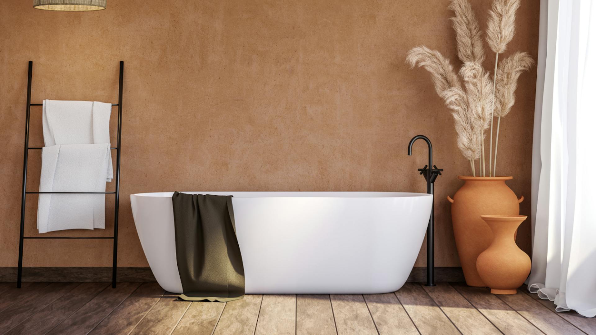 Parete marrone chiaro, davanti una vasca da bagno bianca. Asciugamani bianchi sul portasciugamani a sinistra, erba della pampa a destra in vaso di terracotta.