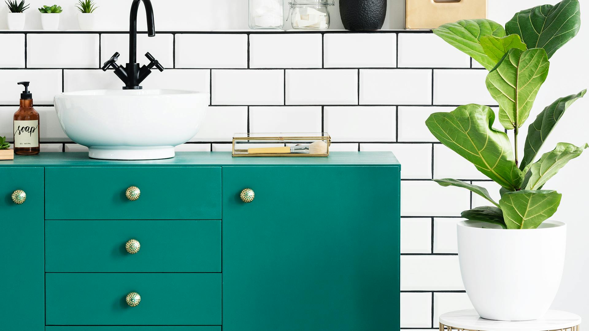 Mobile lavabo turchese su pavimento a piastrelle con motivo a scacchi. Accanto c’è una pianta verde in un vaso bianco.