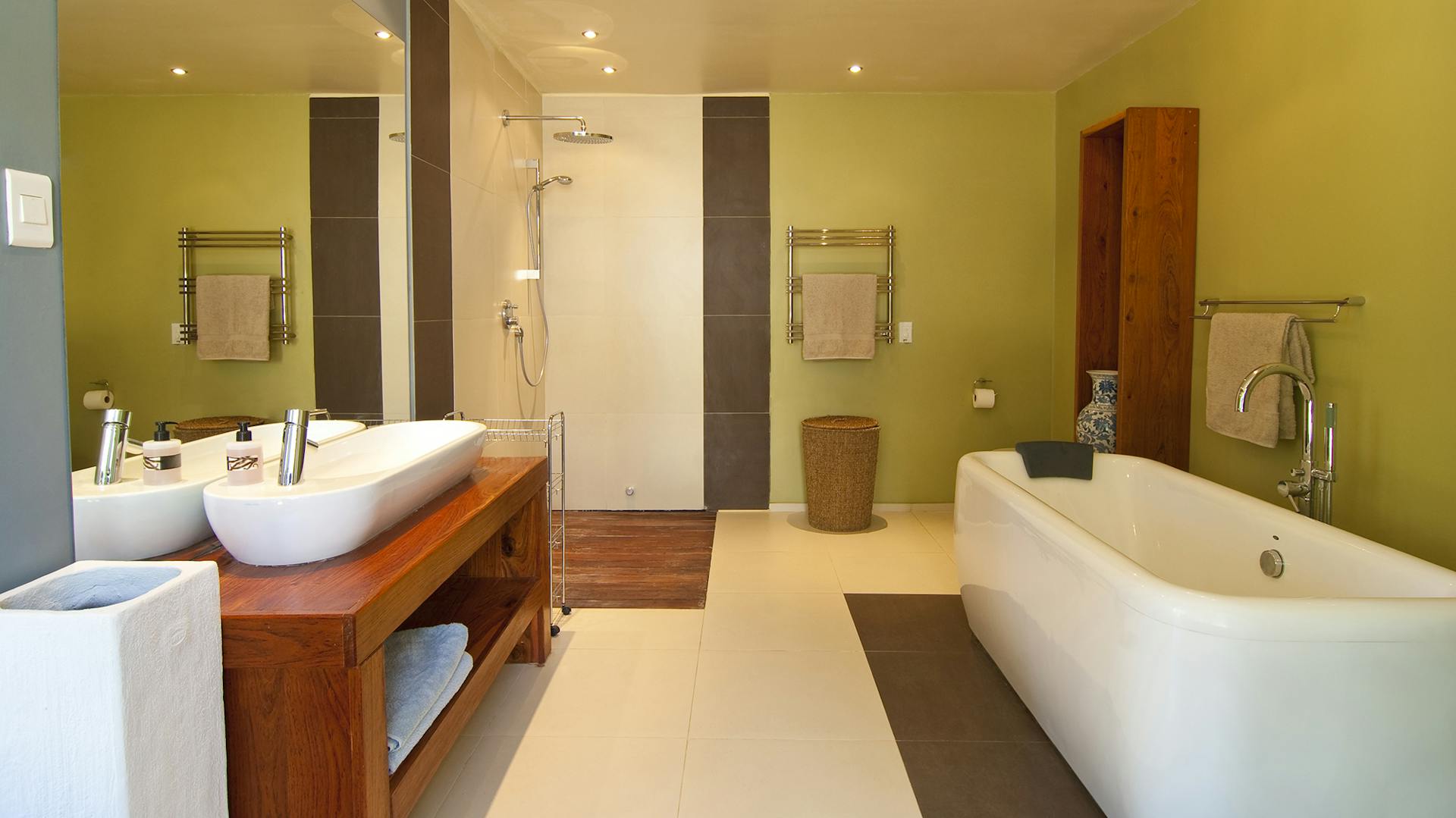 Bagno verde chiaro con mobile lavabo in legno, lavabo bianco e vasca da bagno bianca.