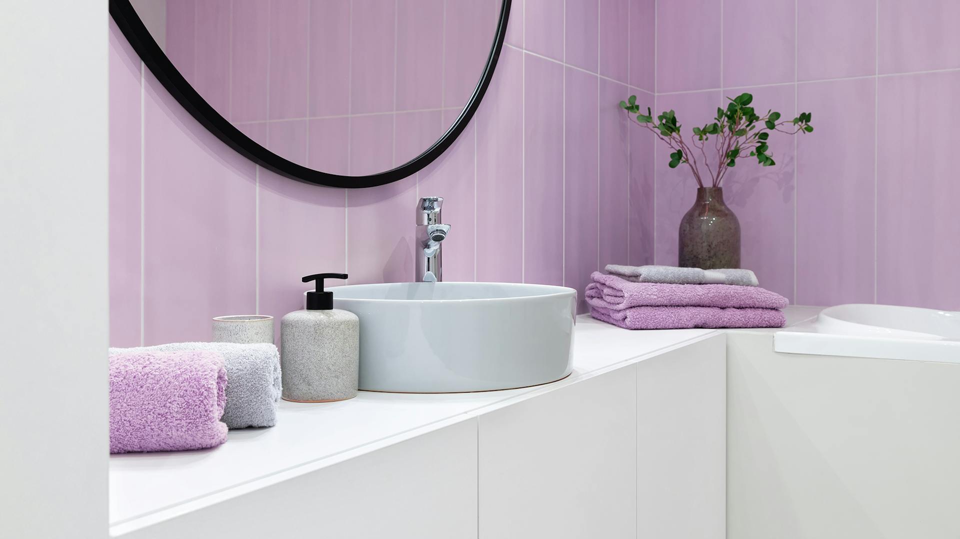 Parete color lavanda, davanti c’è un lavabo rotondo bianco e accessori per il bagno color lavanda.