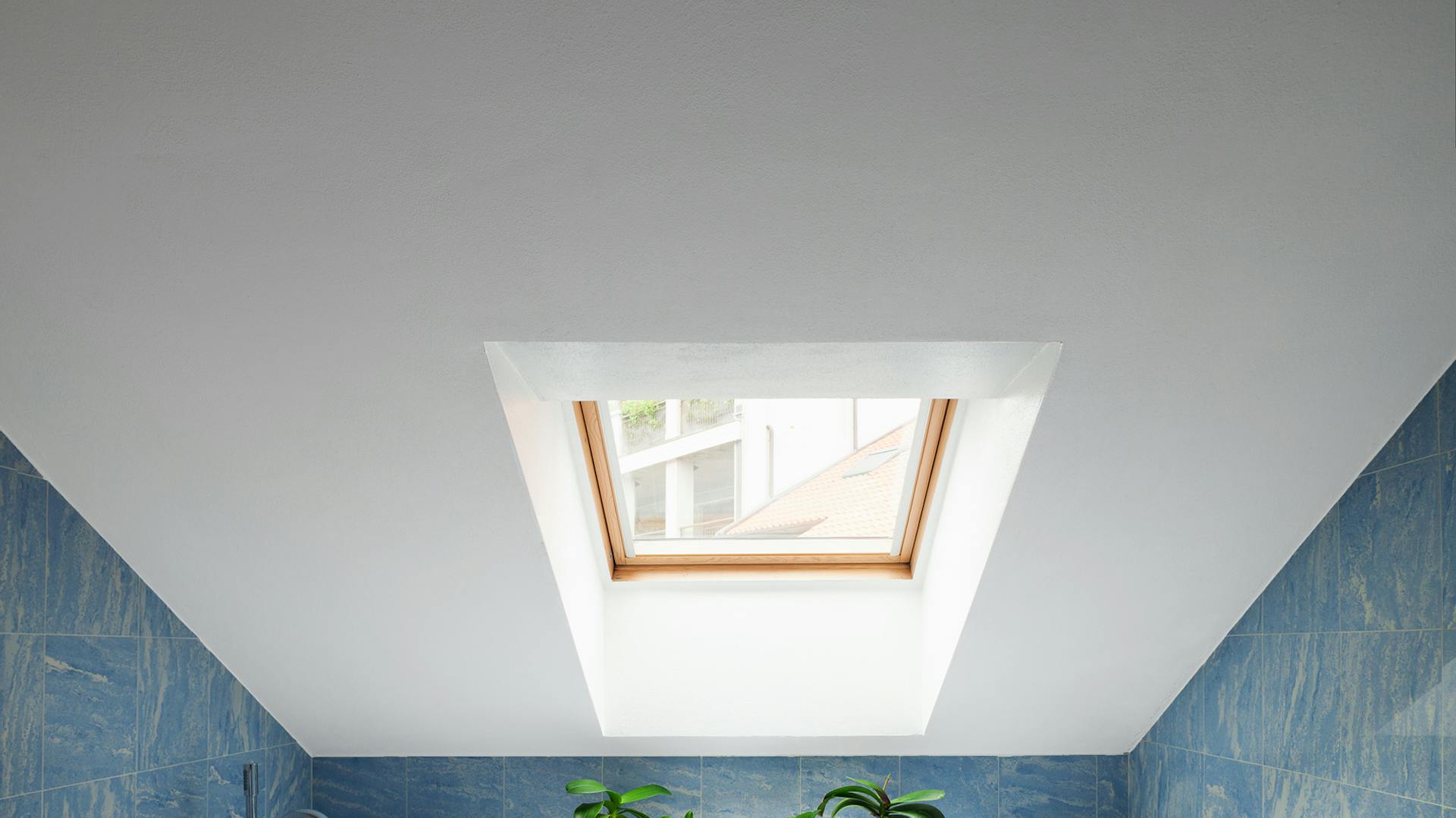 Modře obložená vana pod bíle natřenou šikmou střechou s oknem.