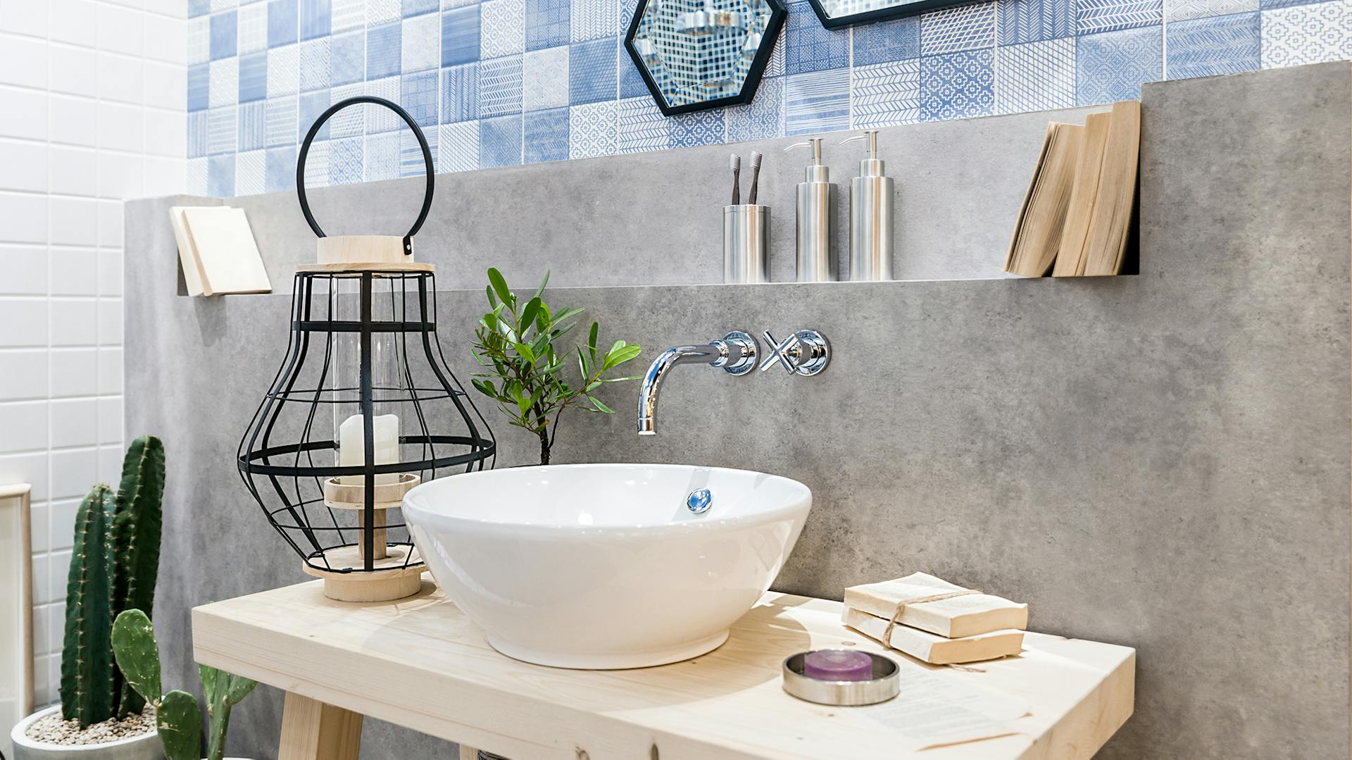 Dřevěná deska s umyvadlem před betonovou stěnou a modrými obklady, rostliny a dekorativní prvky.